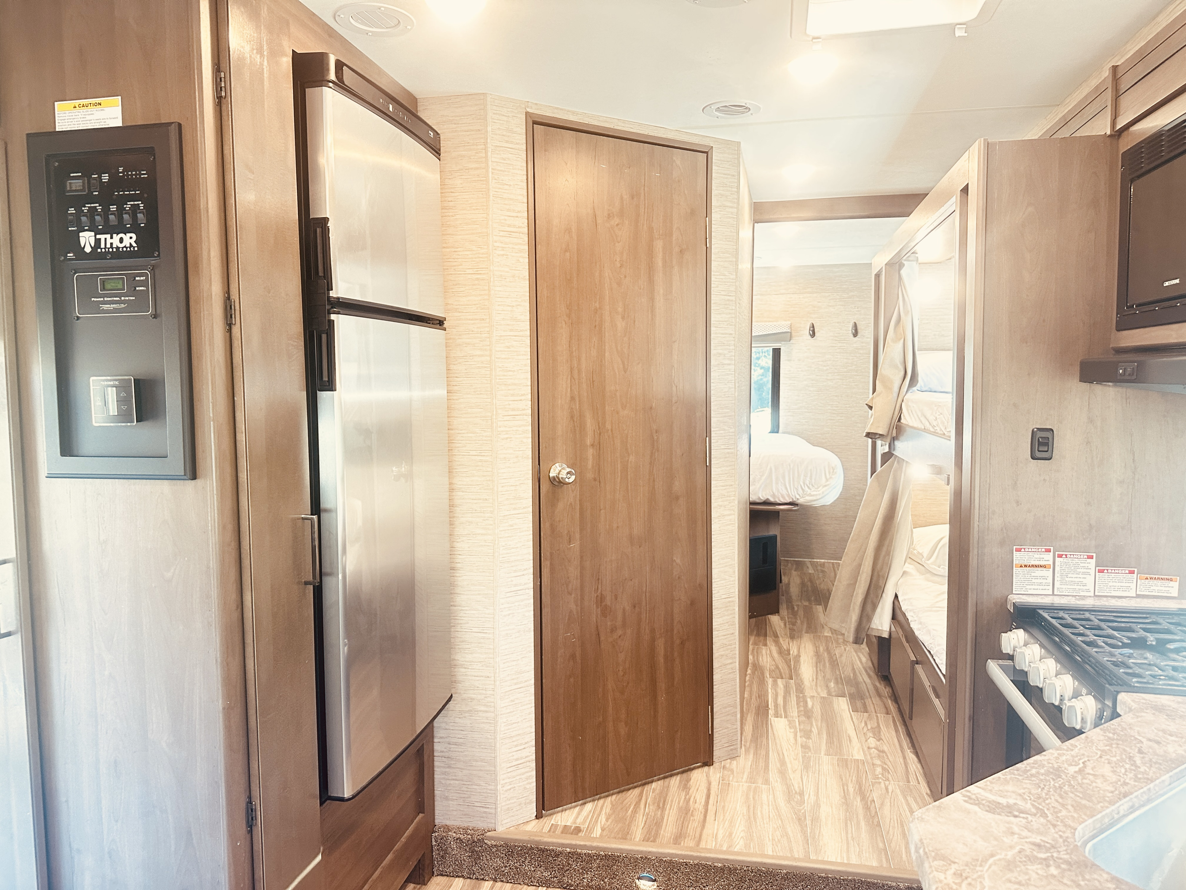 RV rental interior showcases Thor Motor Coach controls, Dometic fridge, kitchen, bunk beds, and a bedroom visible through the doorway.. Thor Four Winds 2022