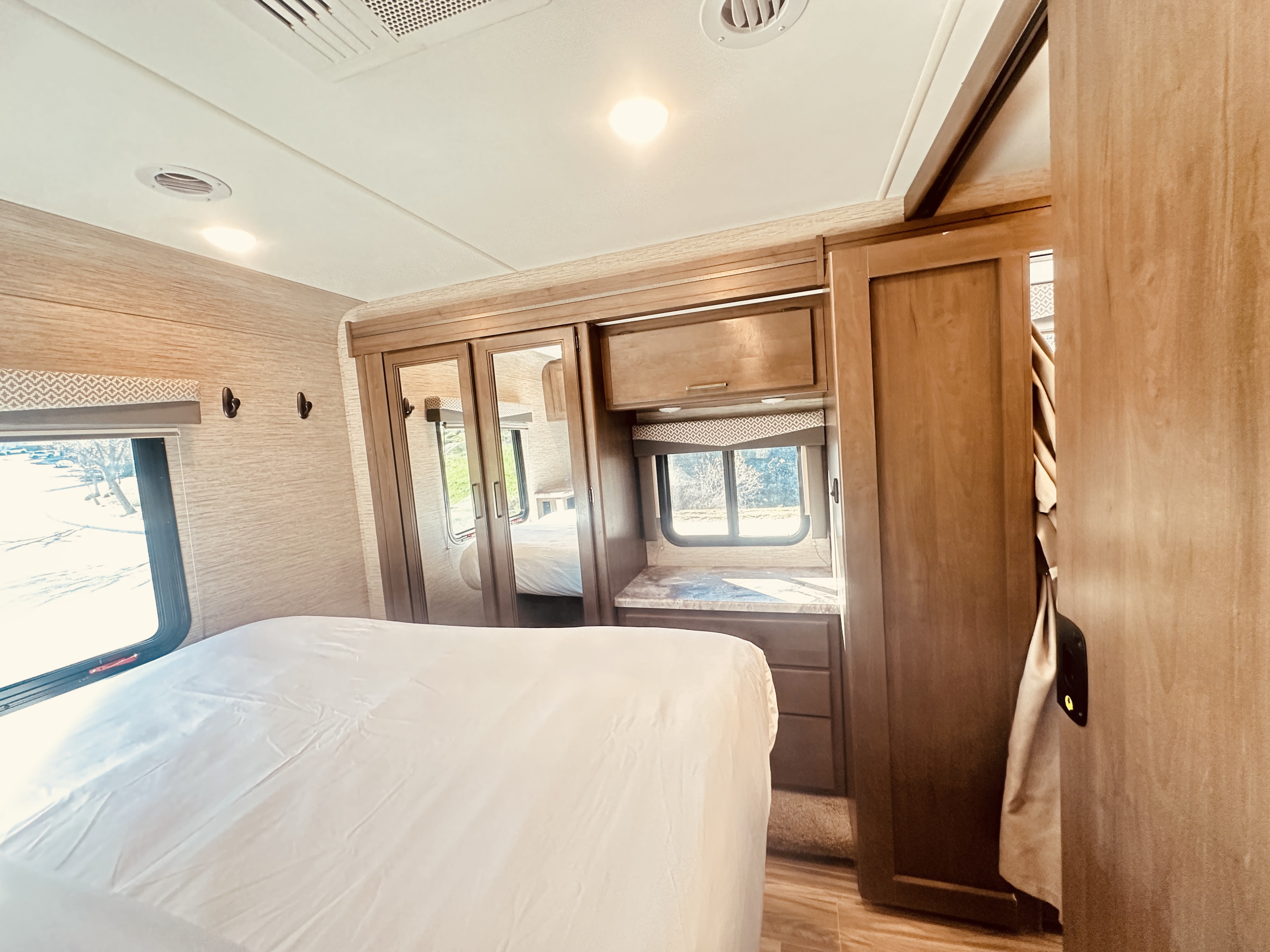 This inviting RV rental bedroom offers a comfortable bed, mirrored closet, dual windows, and wood cabinetry for a cozy journey.. Thor Four Winds 2022