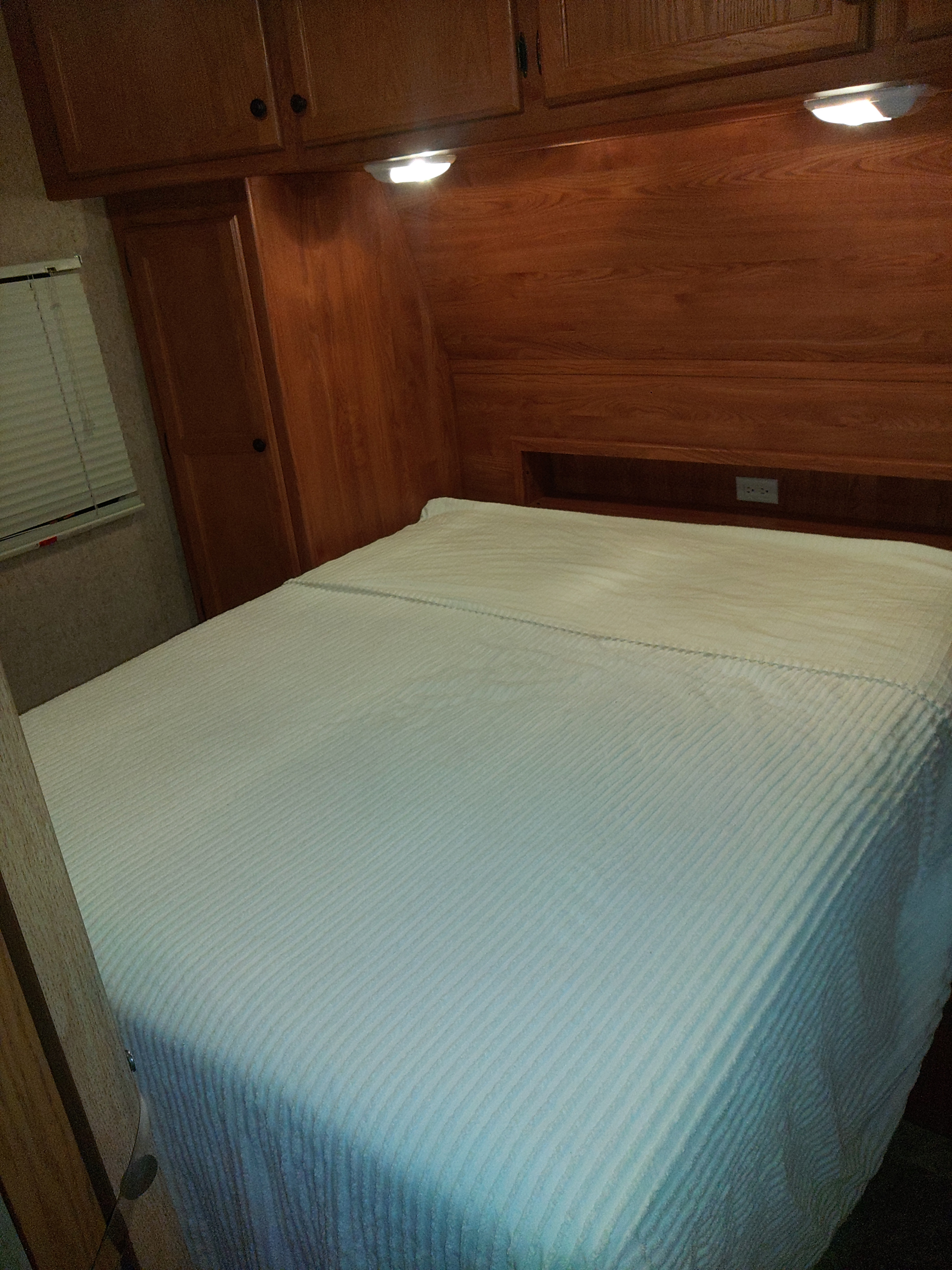 Cozy RV rental bedroom features a neatly made bed with ribbed bedding, warm wooden cabinets, and functional reading lights.. Heartland RVs Trail Runner 2012