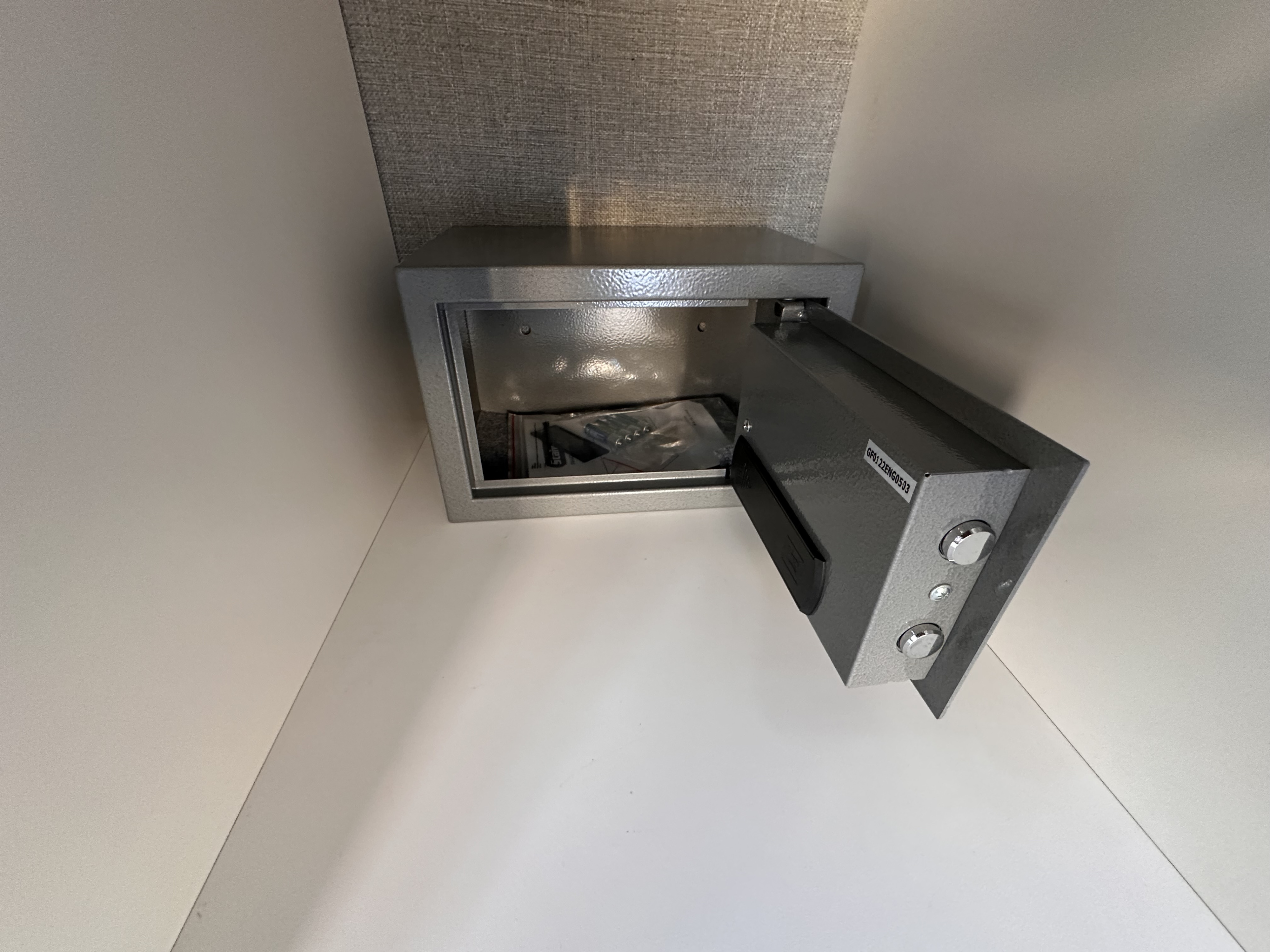 Open grey safe in an RV rental cabinet, containing batteries/manual for secure storage. Keep valuables safe during travel.. Ford Transit 2025