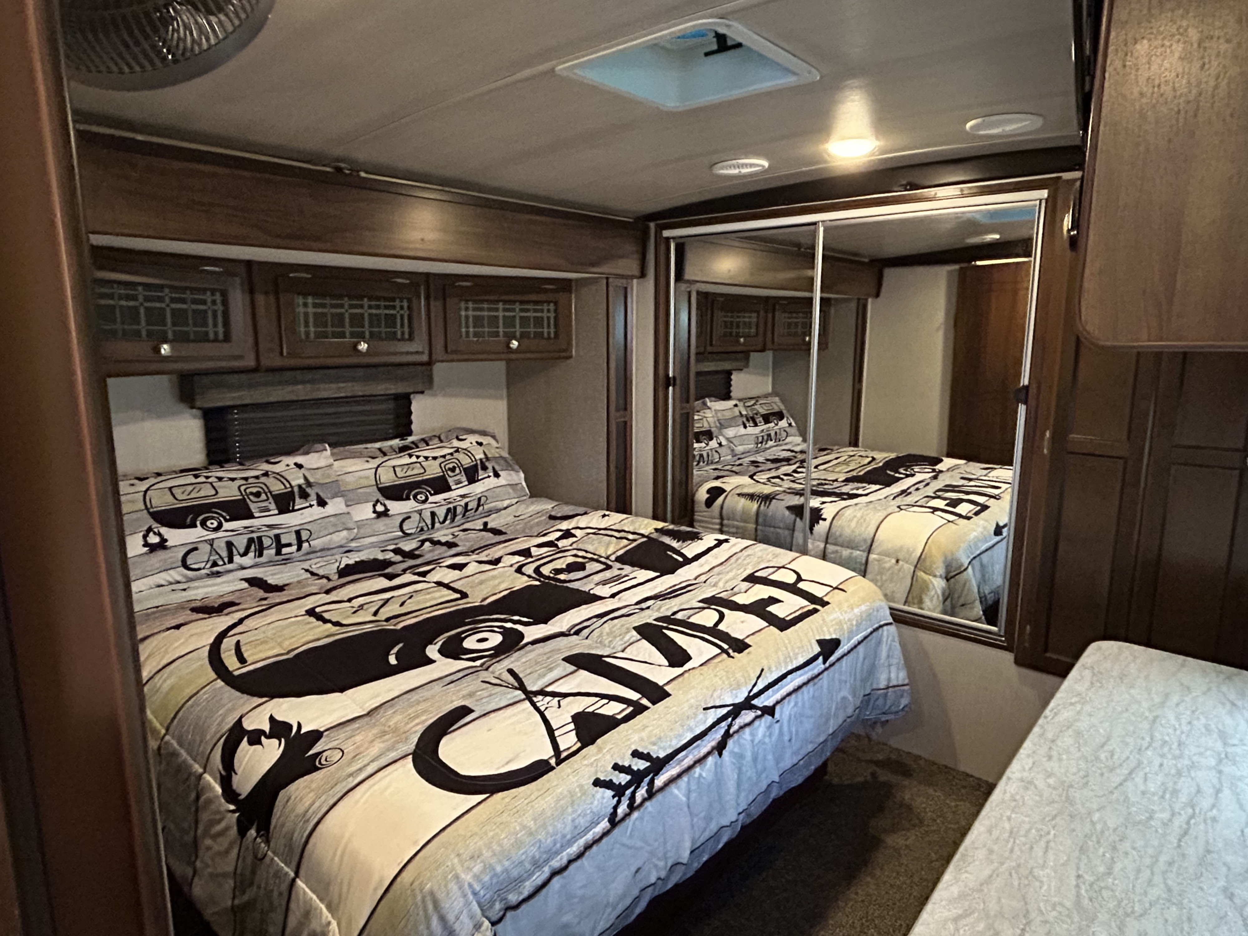 RV rental bedroom with a unique "CAMPER" comforter, wood cabinets, and a large mirrored closet.. Heartland RVs Mallard 2019