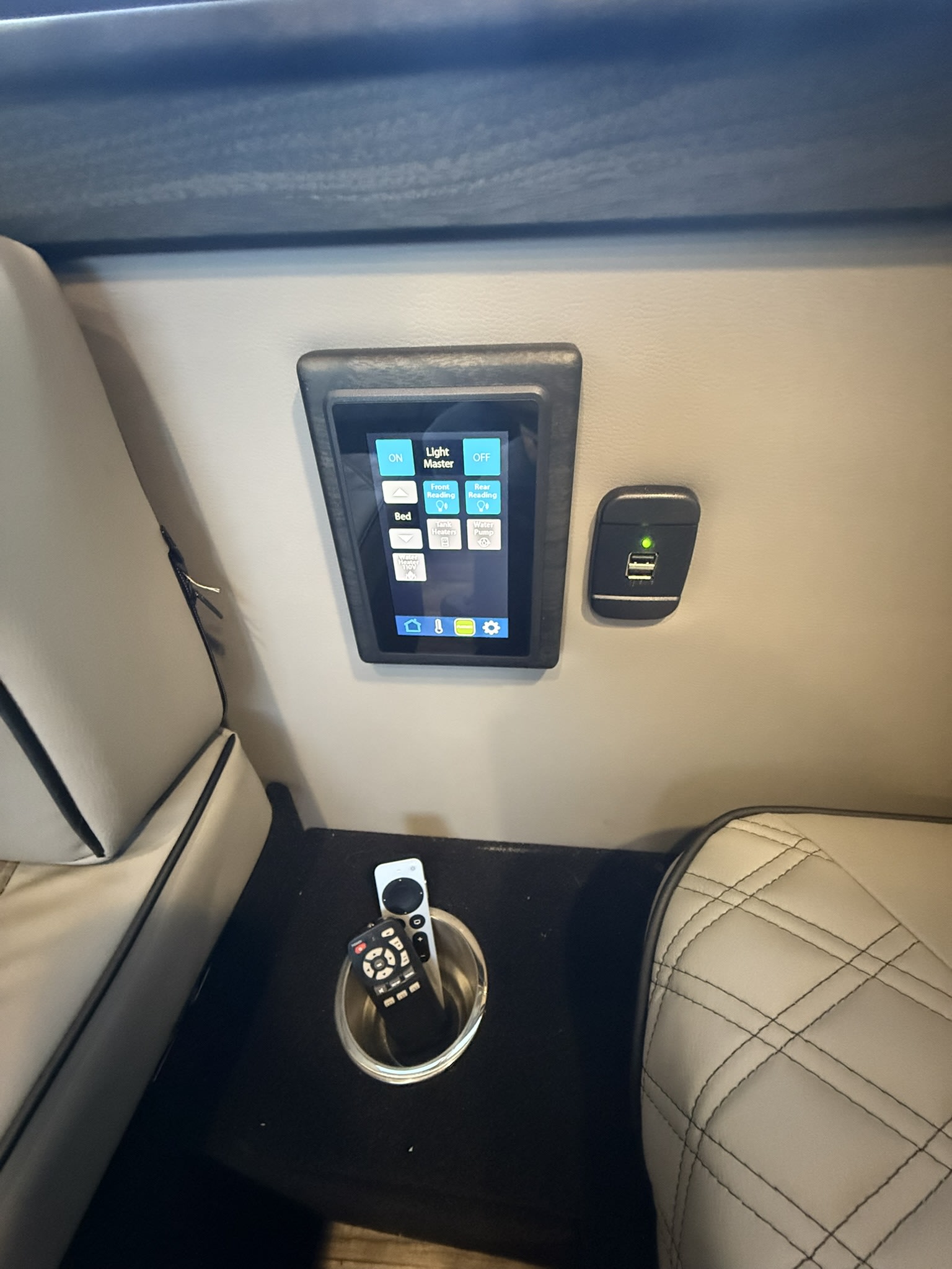 RV rental interior featuring a digital control panel, USB charging port, cup holder with remotes, and comfortable seating.. Midwest Automotive Designs Ultimate CamperVan 2023