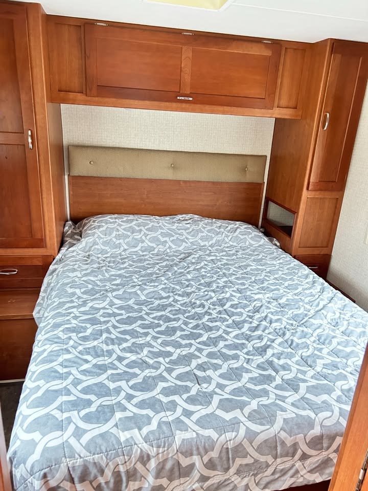 View of an RV rental bedroom with a neatly made bed, wooden overhead storage, and side wardrobes.. Winnebago Minnie Winnie 2018