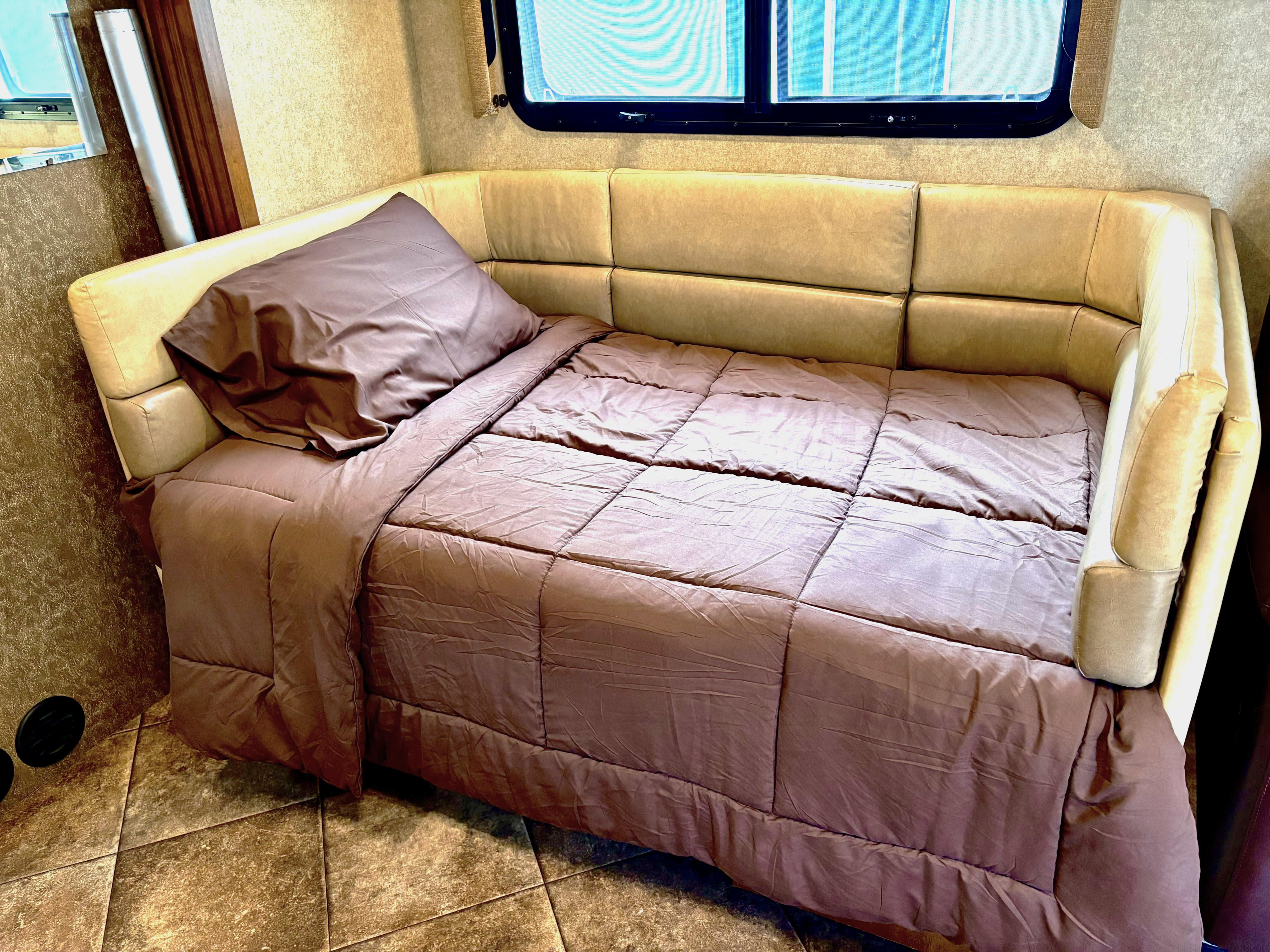 Cozy RV rental sleeping area: brown bed, upholstered tan headboard, and a window above.. A.C.E. A.C.E. Motorhome 2014