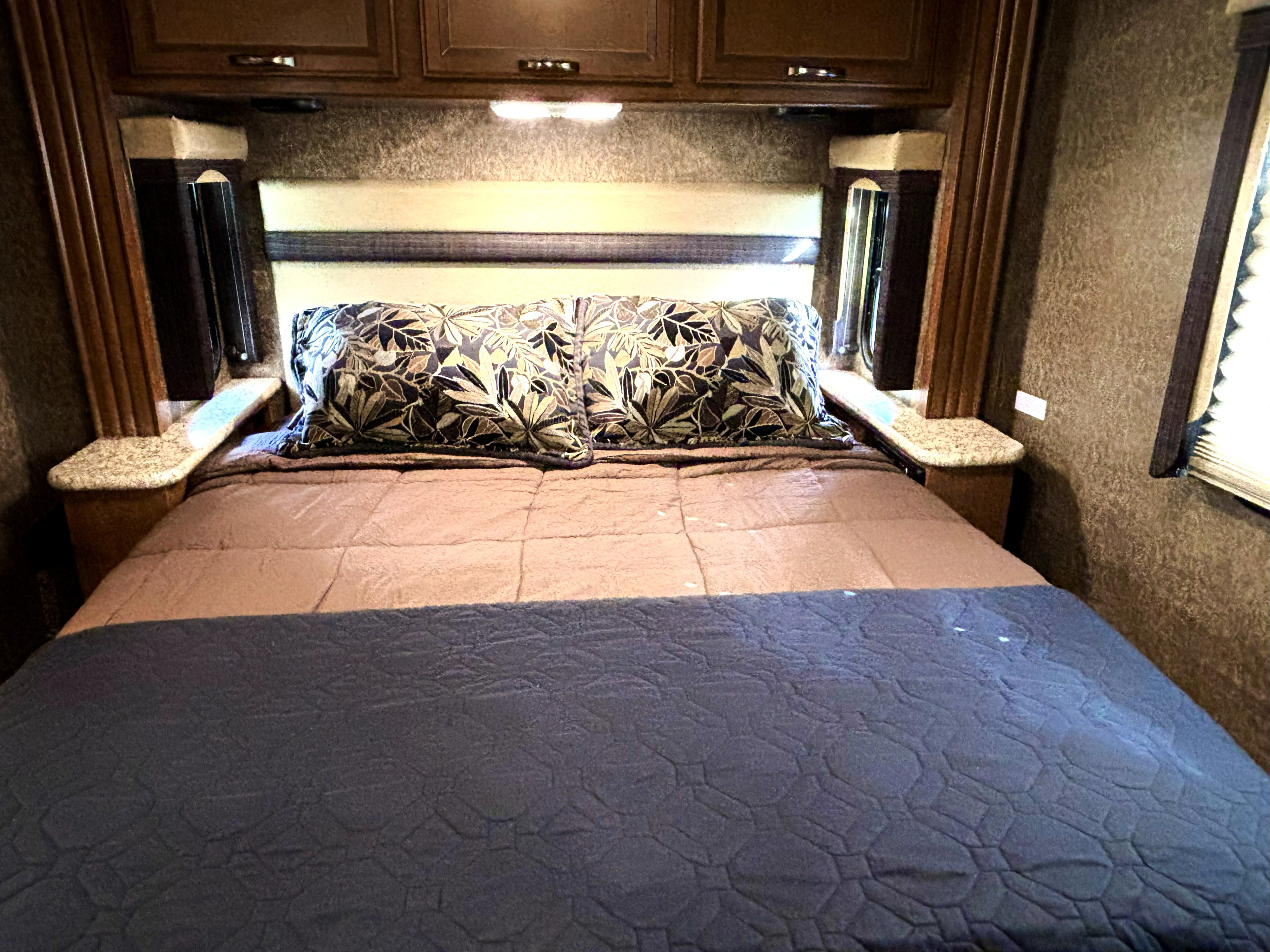 RV rental bedroom: a bed with patterned pillows, a blue blanket, overhead cabinets, and bedside ledges with accent lighting.. A.C.E. A.C.E. Motorhome 2014
