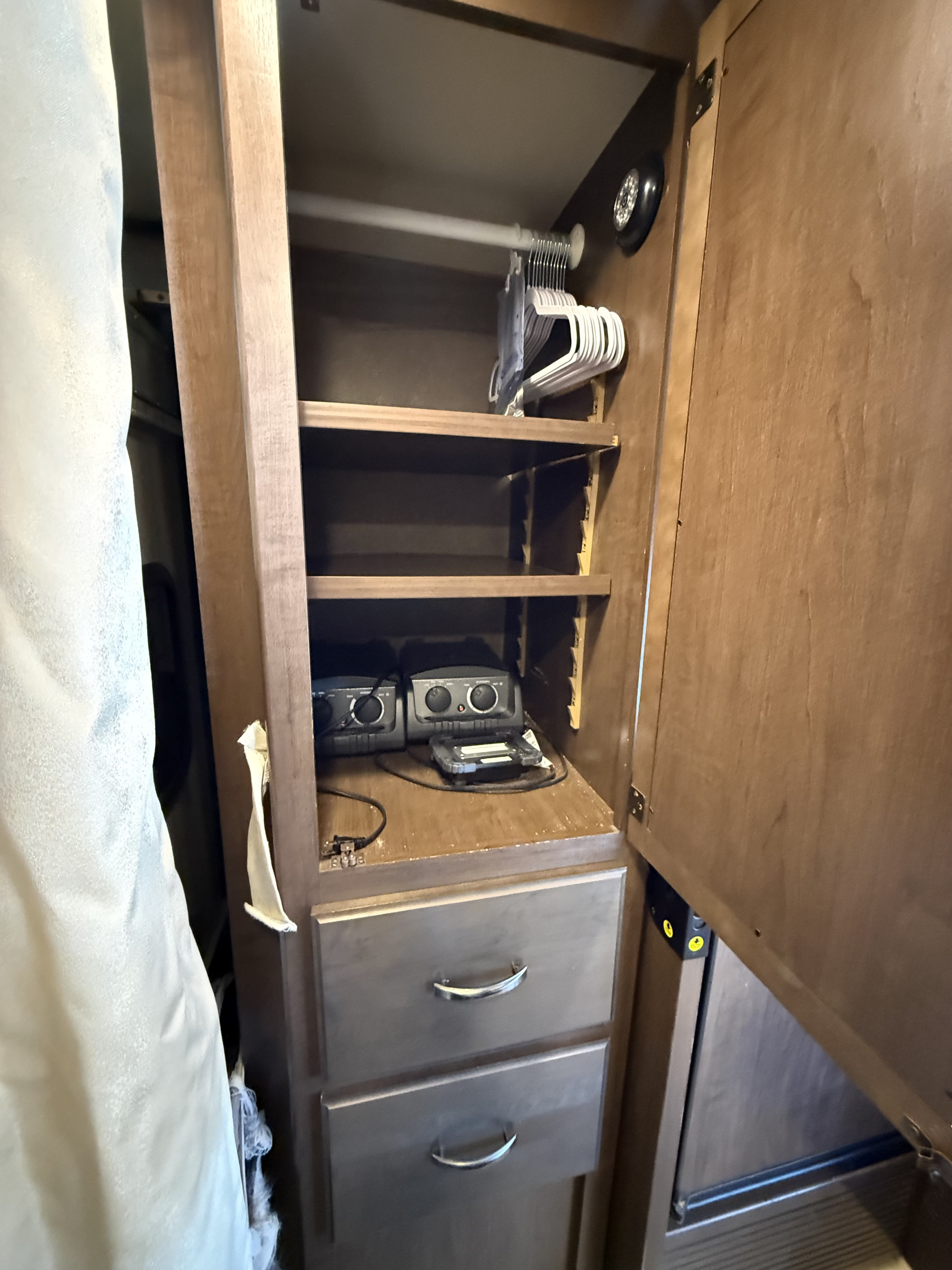 RV rental interior: open wardrobe with shelves, hangers, and drawers, showing compact storage and electronic devices.. Thor Vegas 2017