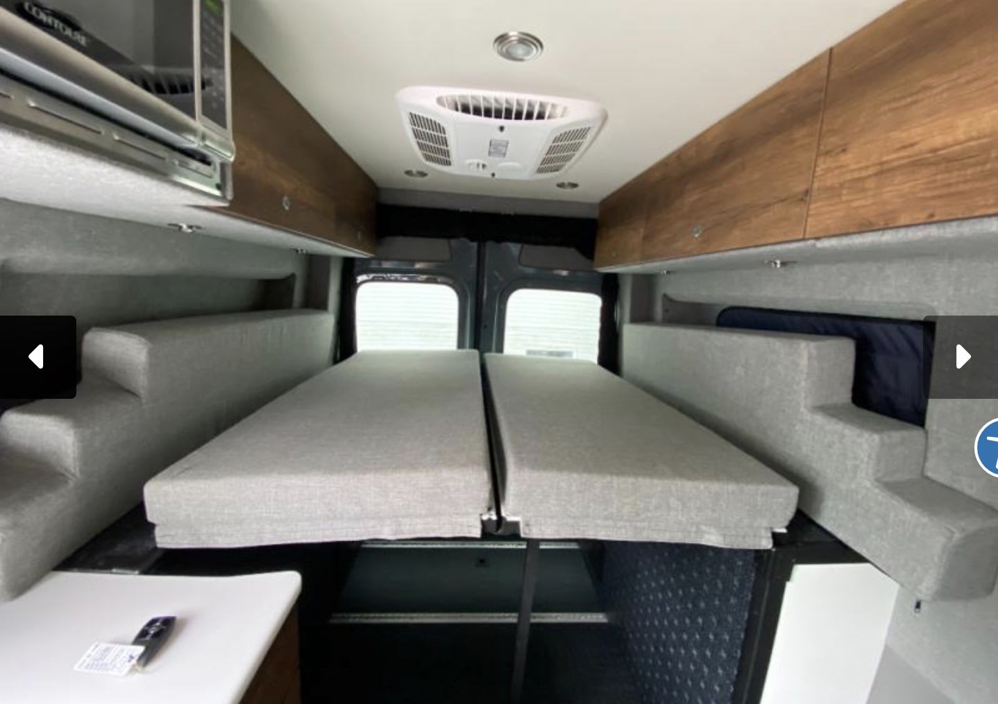 RV rental interior featuring a cozy bed, overhead storage, microwave, and AC unit for comfortable travels.. Storyteller Overland Storyteller Overland Class B 2021