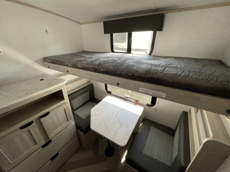RV rental interior: A cozy upper bunk bed hangs over a dinette with a table and benches. Storage drawers are on the left. Compact design.. Cruiser RV Shadow Cruiser 2021