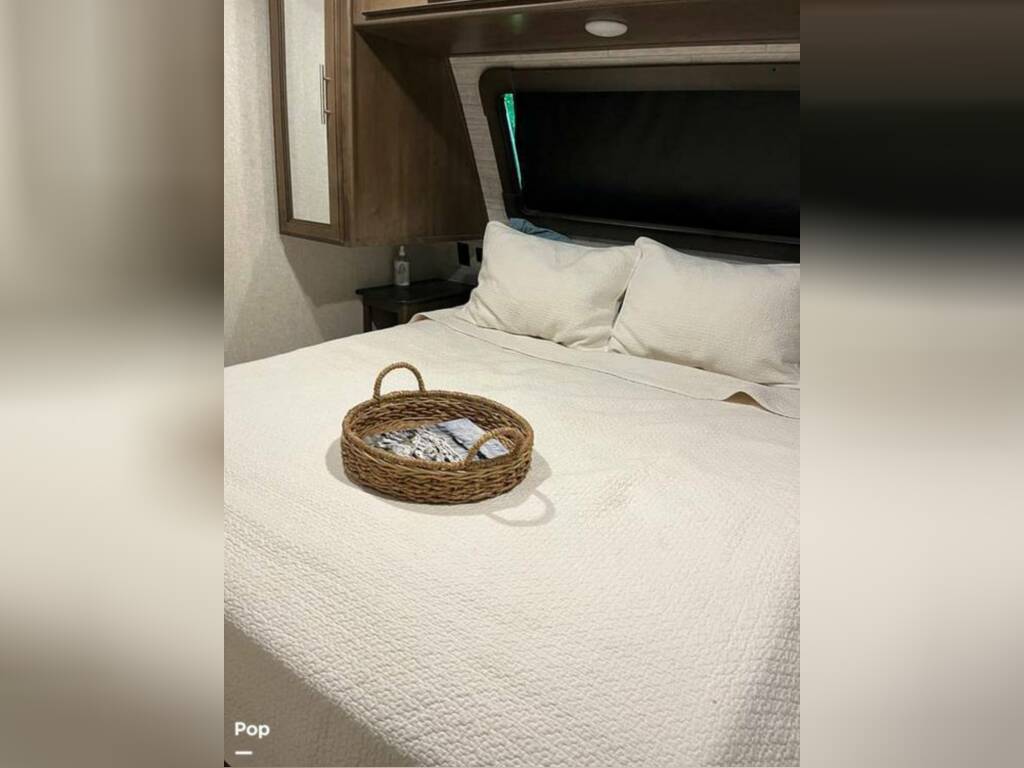 Cozy RV rental bedroom features a bed with white bedding, pillows, and a decorative basket, perfect for comfortable travel.. Keystone RV Cougar 2021
