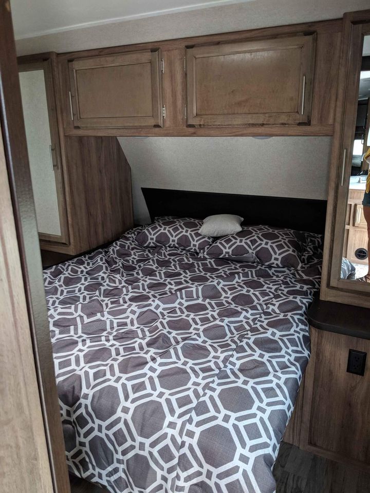 RV rental bedroom interior featuring a bed with geometric patterned bedding, overhead cabinets, and side storage.. Jayco Jay Feather 2019