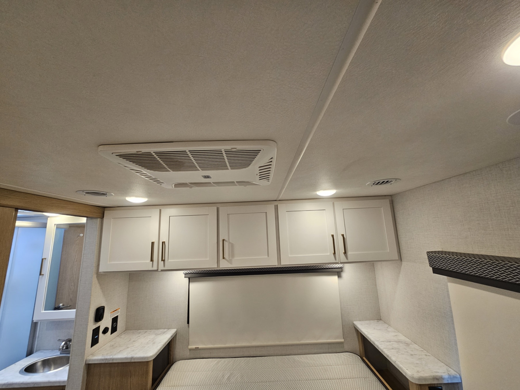 Interior of an RV rental bedroom with white overhead cabinets, an AC unit, and a glimpse of a bathroom on the left.. Thor Motor Coach FourWinds 2026
