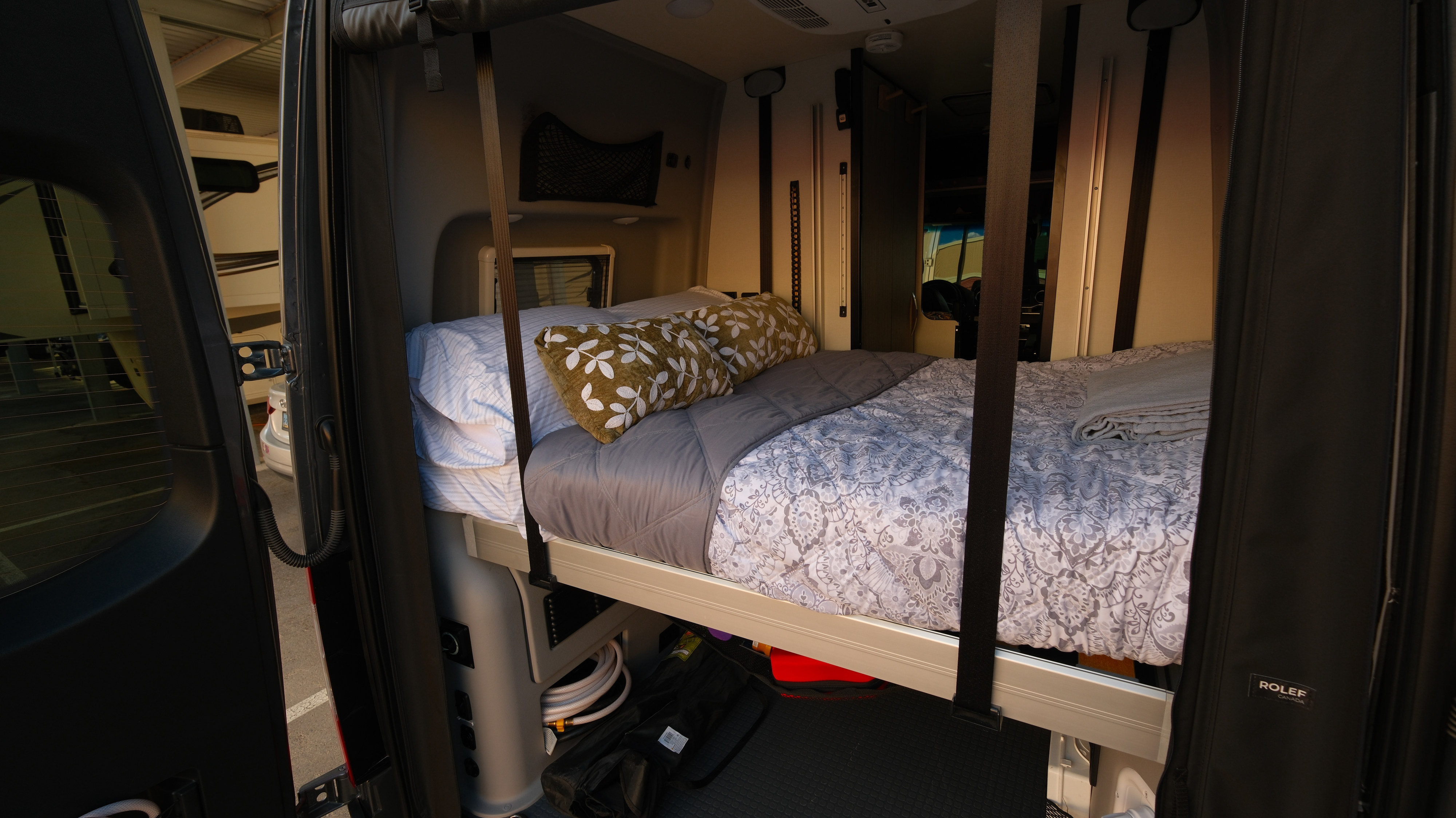 Inside a comfortable RV rental, featuring a made-up bed and storage, seen through the open rear doors.. Mercedes Winnebago 2024