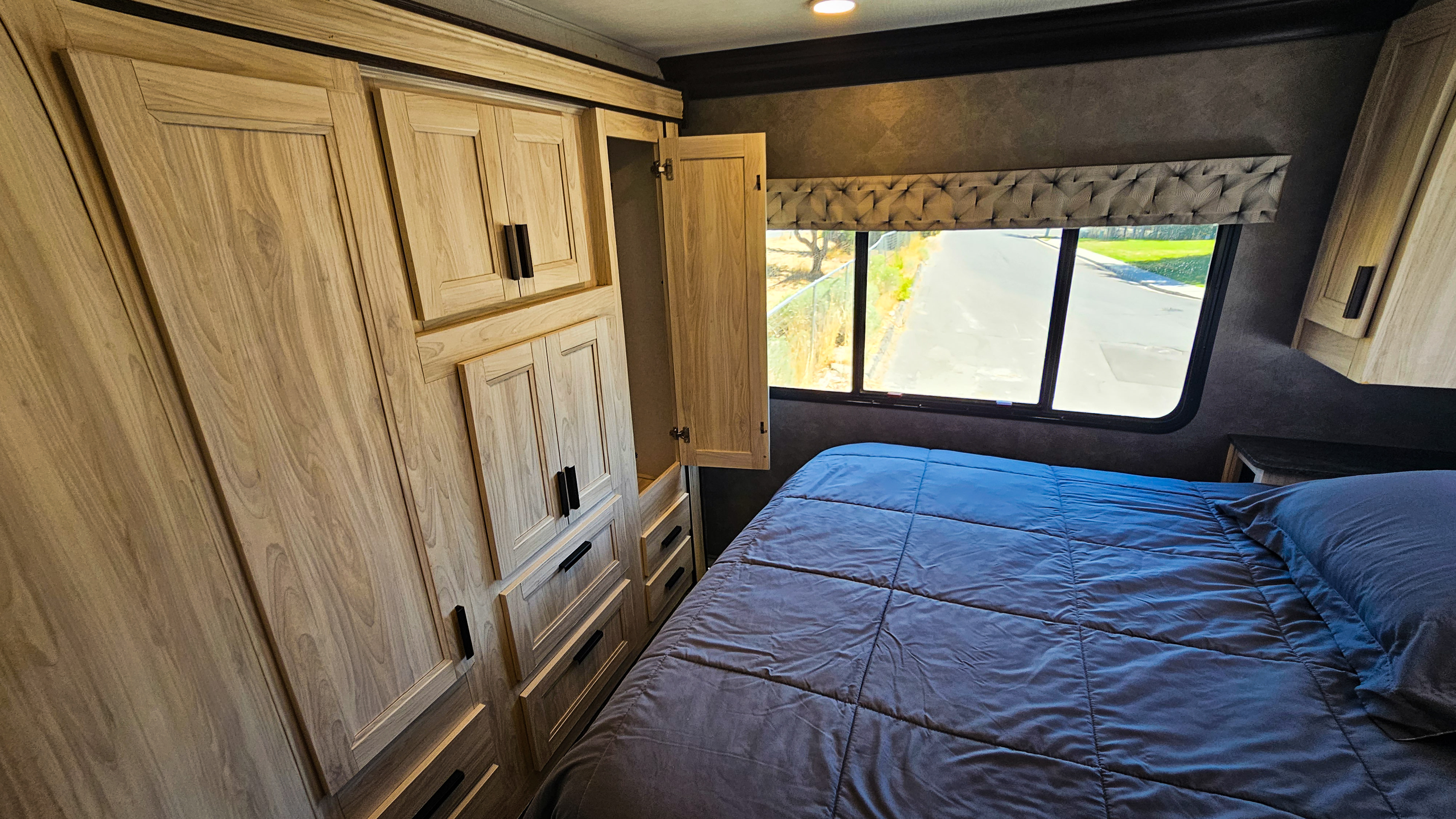 Spacious RV rental bedroom featuring a dark blue bed, ample built-in wooden storage cabinets, and a window with a road view.. Forest River Sunseeker LE 2022