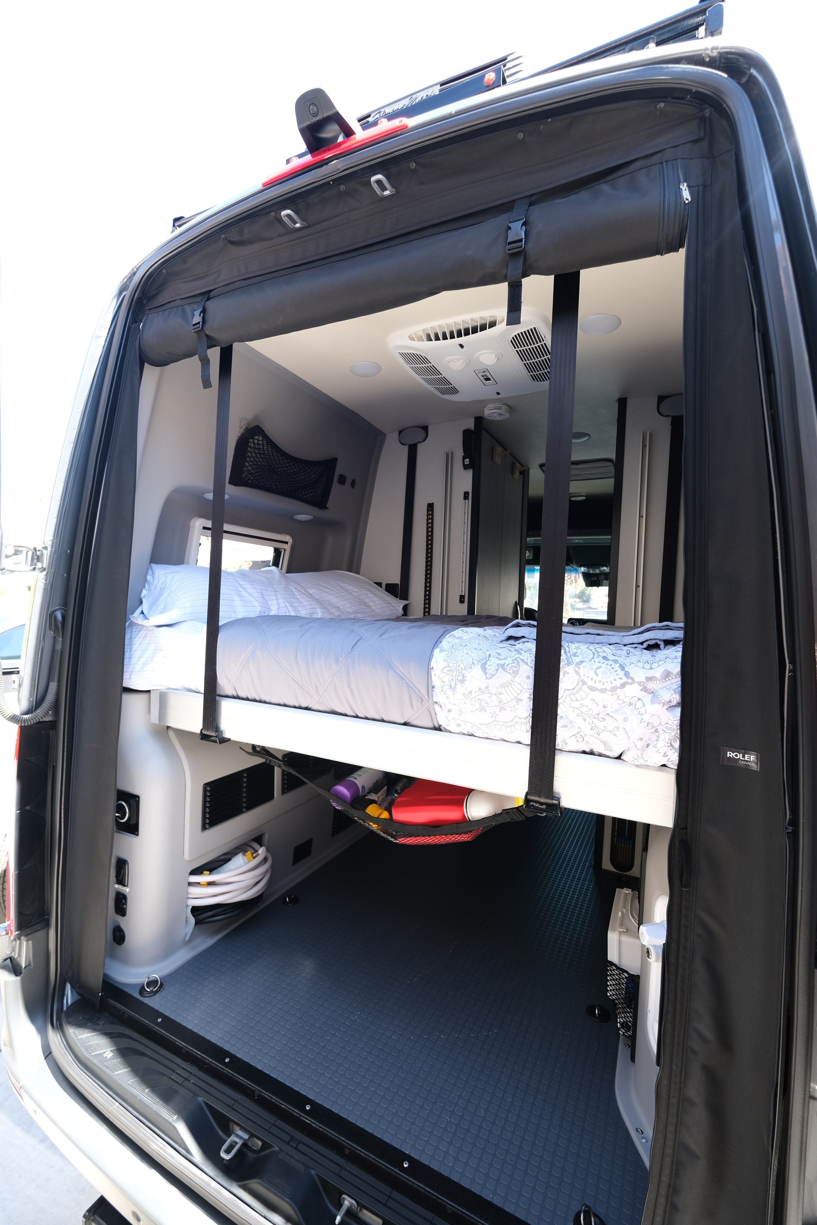 Rear view of an RV rental's clever interior, showcasing a raised bed, under-bed storage, and air conditioning unit.. Mercedes Winnebago 2024