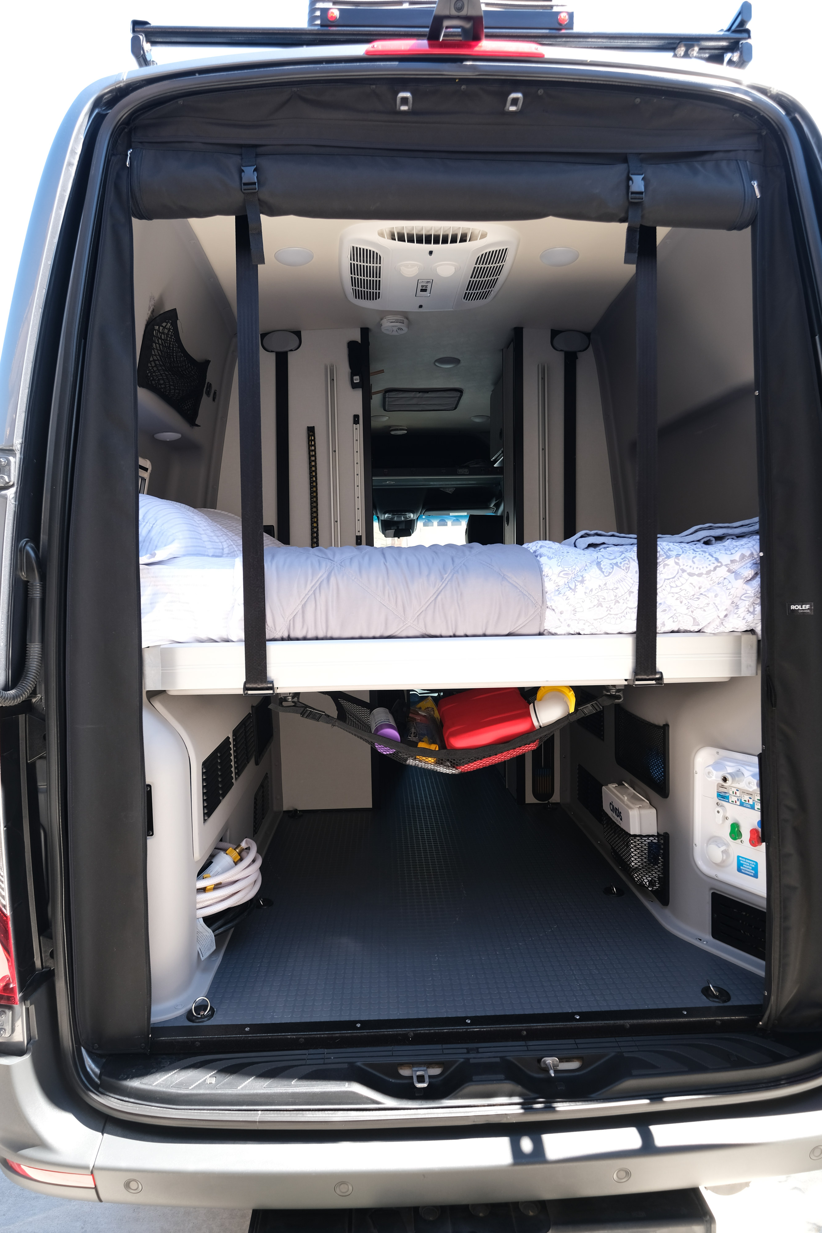 Rear view of an rv rental camper van interior: elevated bed, storage with hose & gear, utility panel.. Mercedes Winnebago 2024