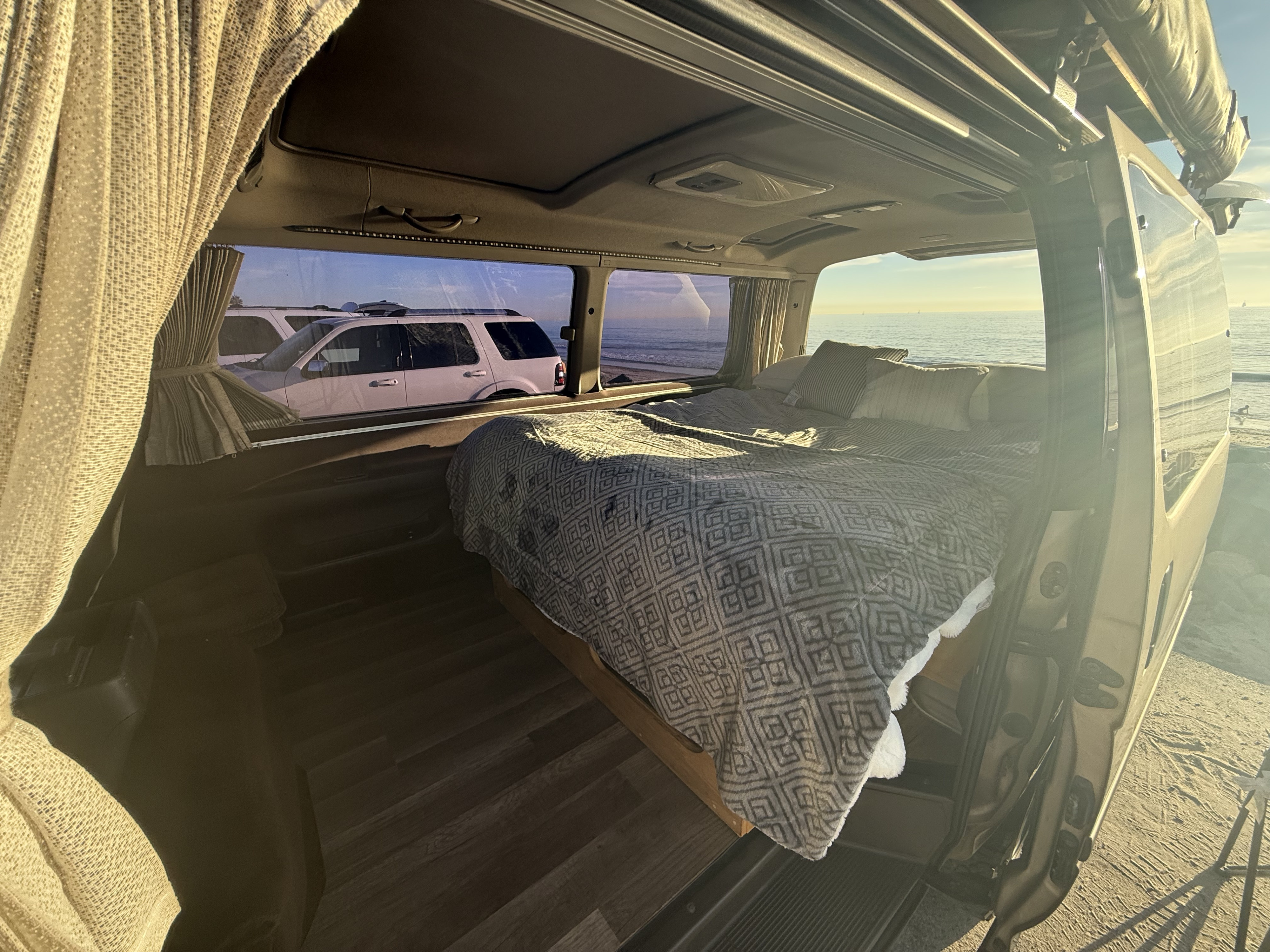 This RV rental offers a cozy campervan interior with a bed, wood floor, and stunning ocean views for your travel adventures.. Toyota Hiace 4WD 1994