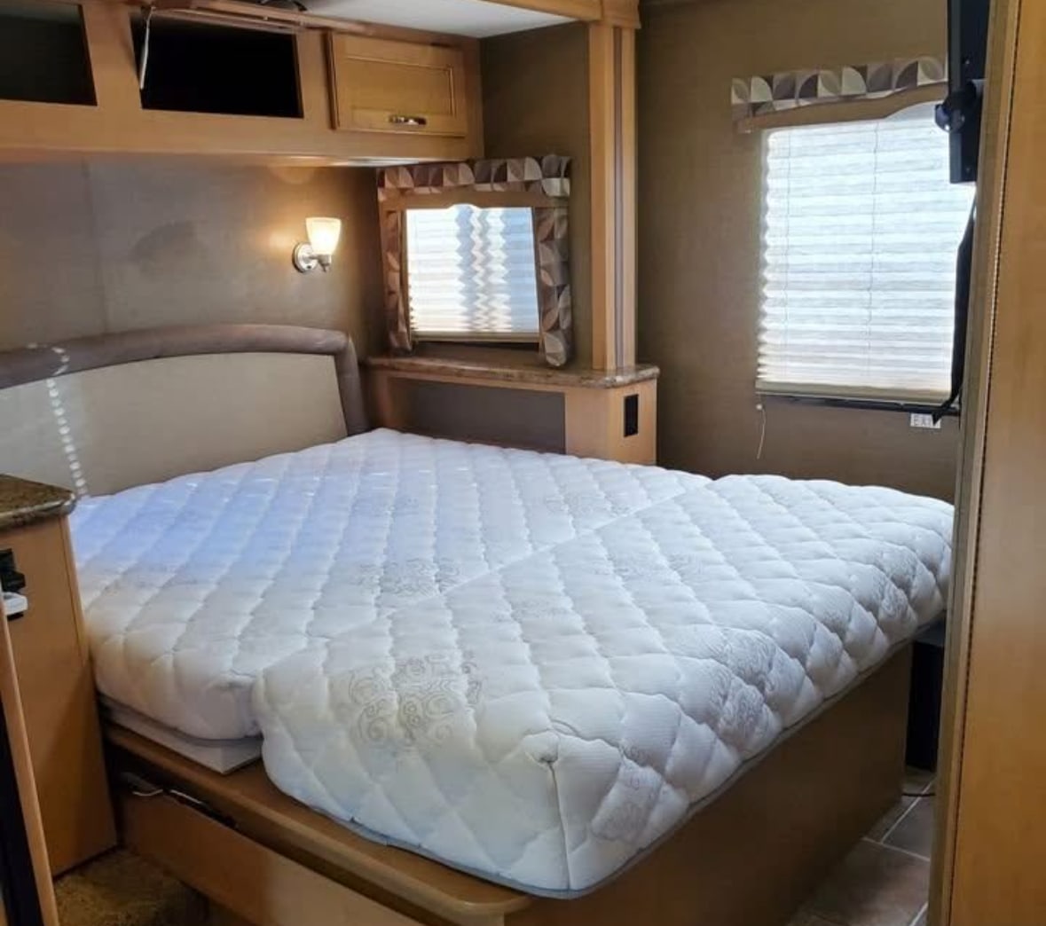 Experience comfort in this RV rental's bedroom, featuring a plush, white mattress, overhead storage, and a window with blinds.. Thor Chateau 2016
