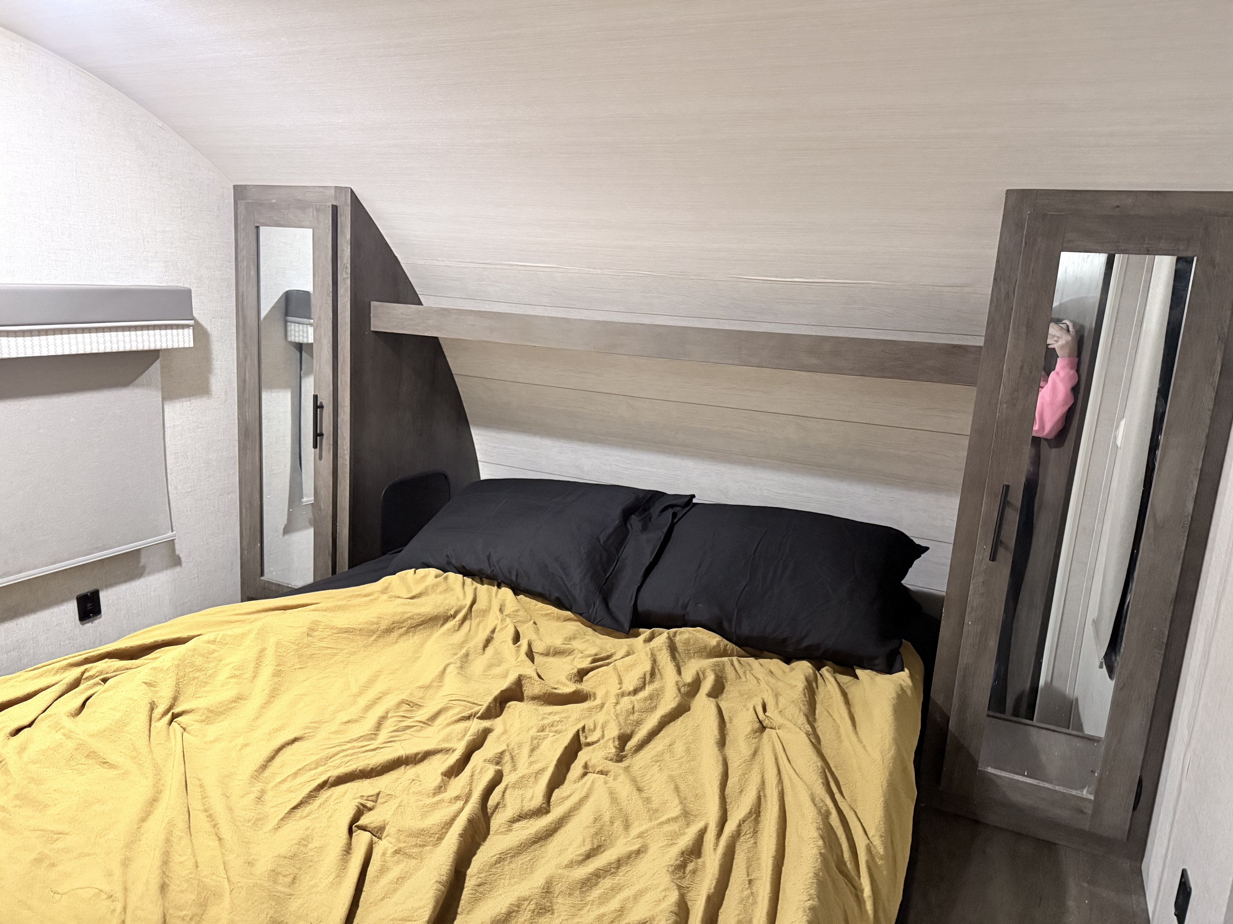Cozy rv rental bedroom with a yellow comforter, black pillows, mirrored cabinets, and a compact headboard shelf.. Forest River Wildwood X-Lite 2021