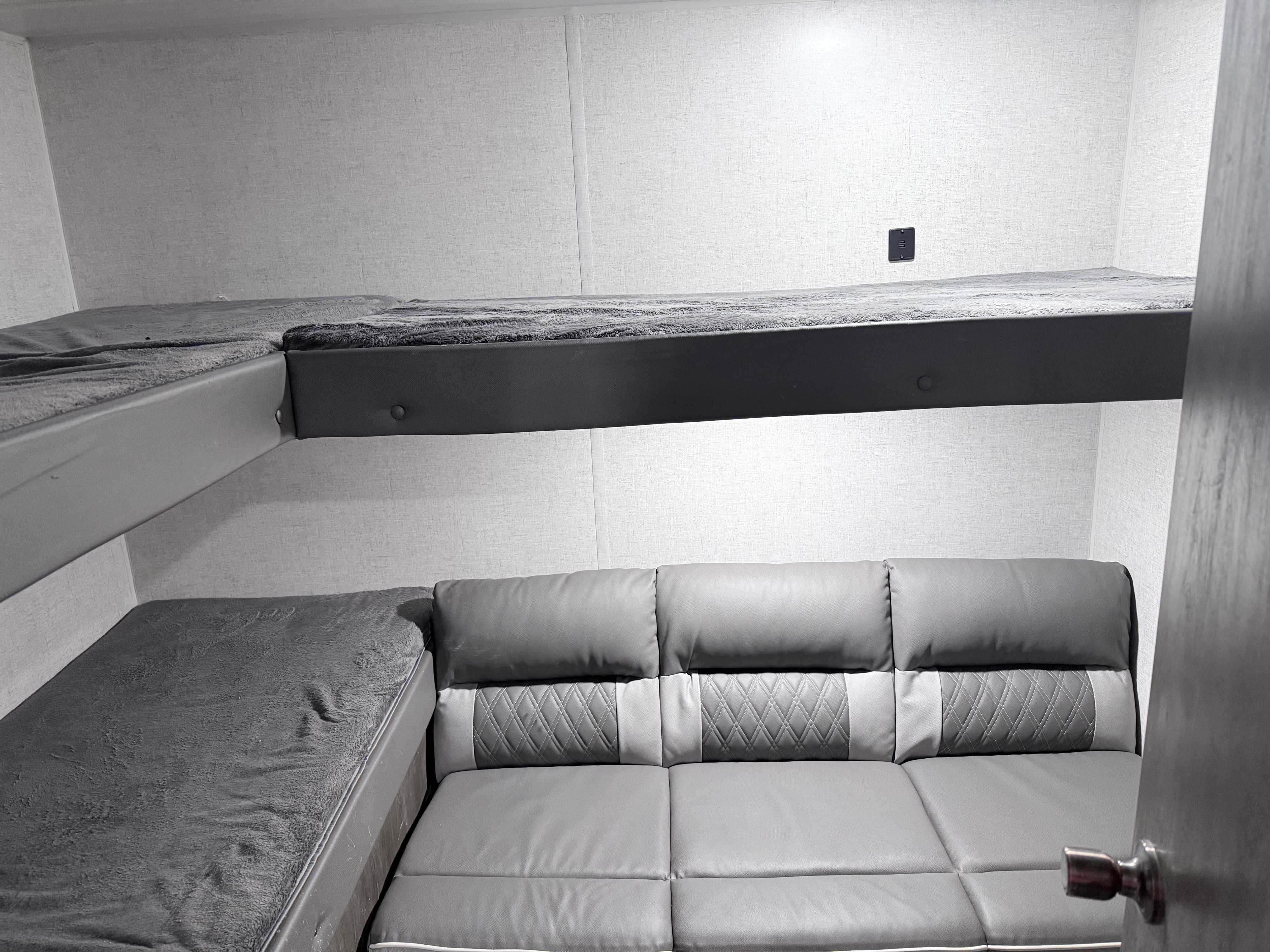 Inside this RV rental: two gray bunk beds with soft blankets, and a sleek gray sofa below. A cozy, compact sleeping & living space.. Forest River Wildwood X-Lite 2021