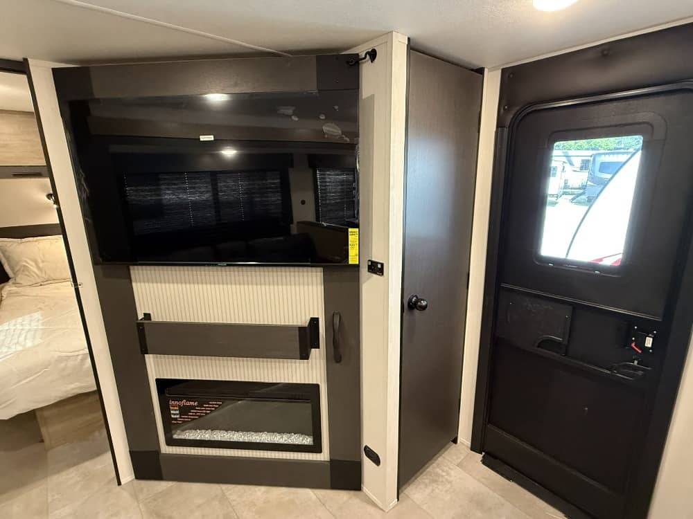 Explore this RV rental's modern interior featuring a TV, electric fireplace, entry door, and a glimpse of the bedroom.. Forest River Campsite Reserve 2026