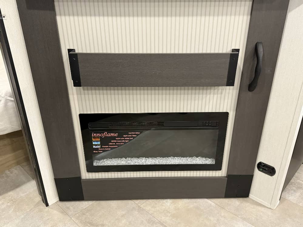 Inside a modern RV rental: a built-in electric fireplace with crystal embers, framed in dark wood-look trim.. Forest River Campsite Reserve 2026