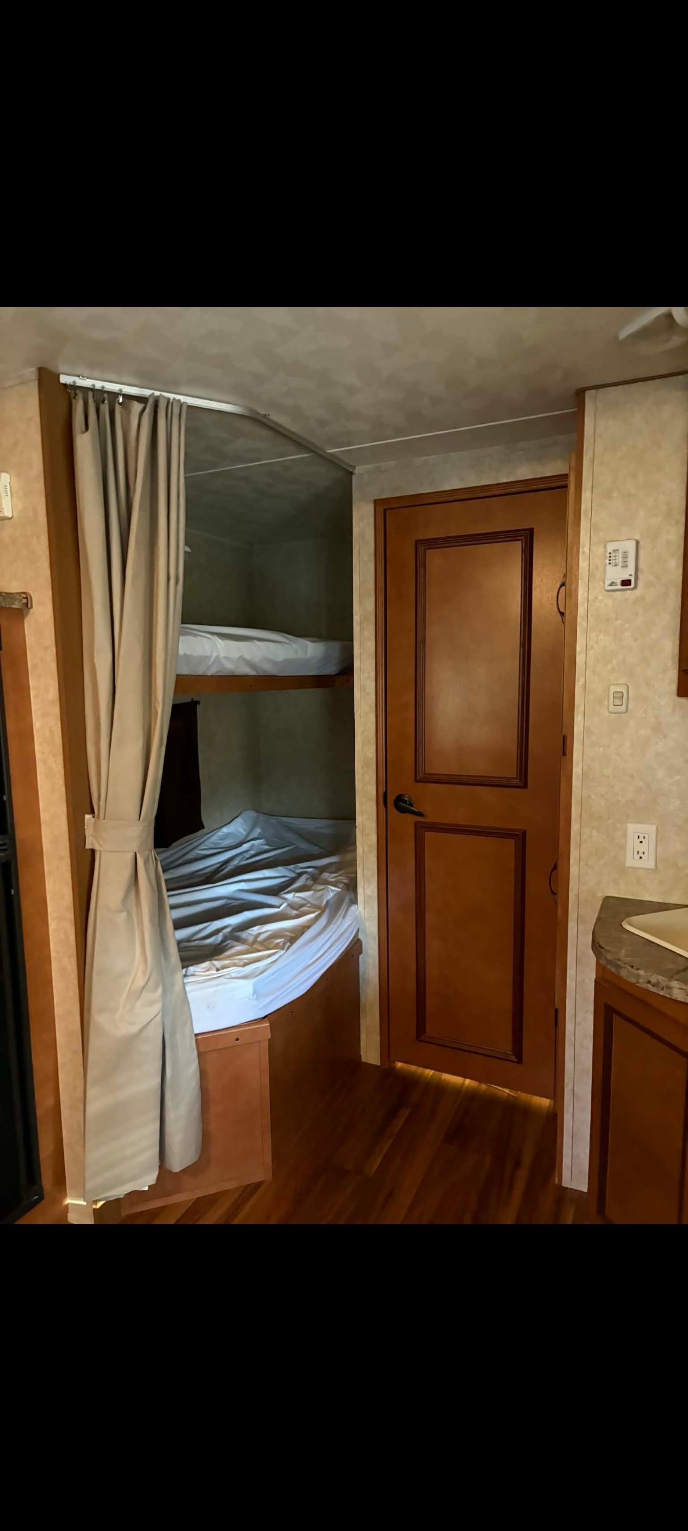 RV rental interior: cozy bunk beds with a privacy curtain and wooden door, ideal for family travel.. Gulf Stream Conquest-Lite 2012