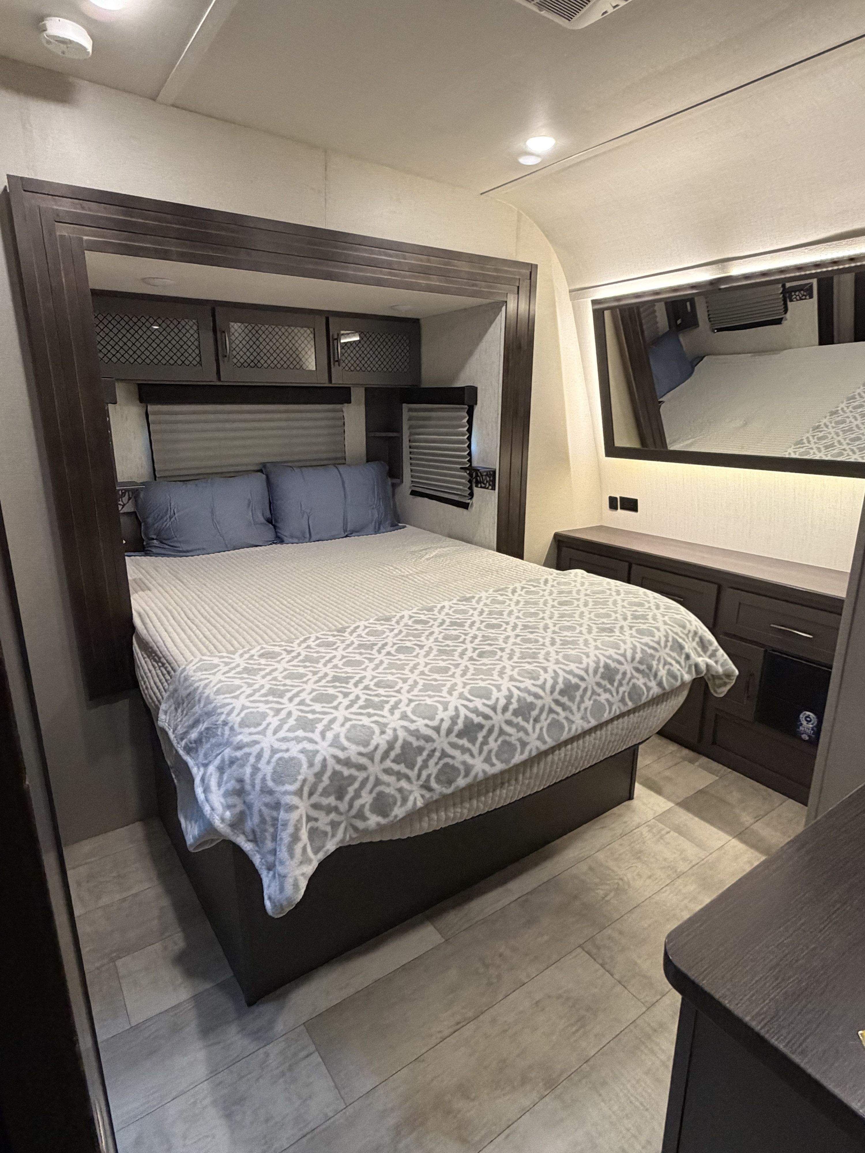 Cozy RV rental bedroom with a comfortable bed, dark wood furniture, light flooring, and a mirrored wall.. Grand Design Momentum 2022