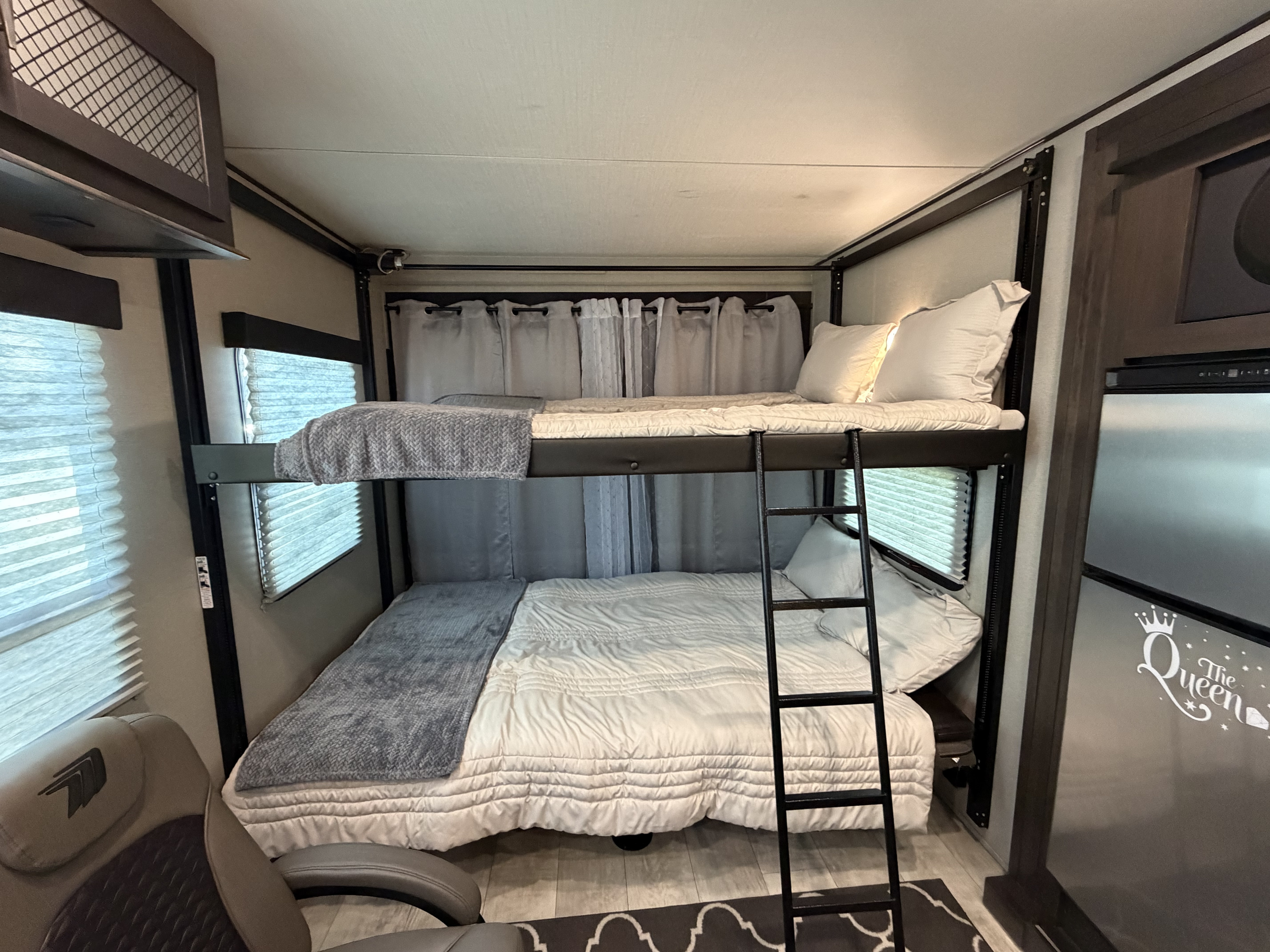 View inside an RV rental showing stacked bunk beds, complete with white bedding, gray blankets, and a ladder.. Grand Design Momentum 2022