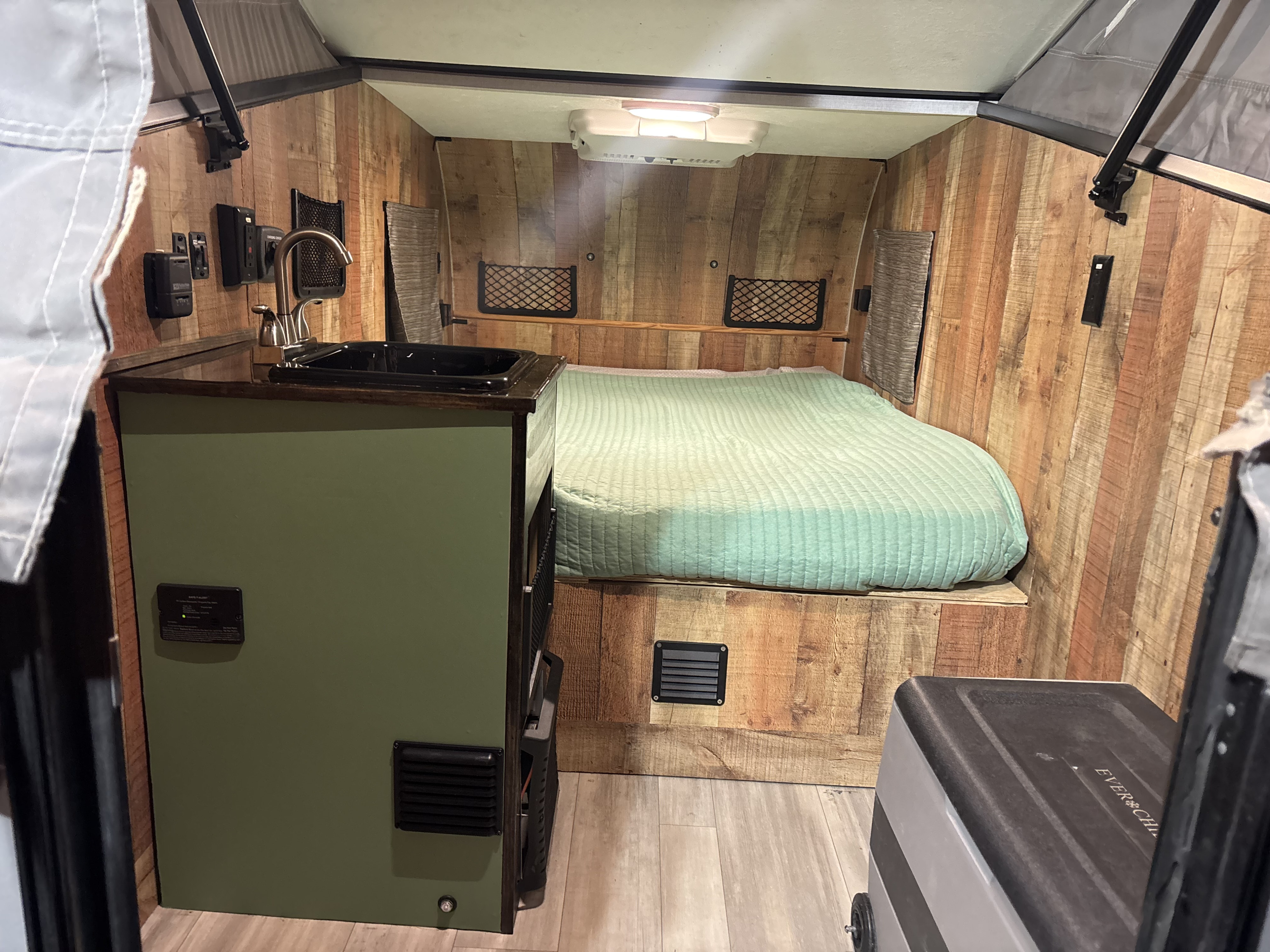 Cozy rv rental interior: green bed, small kitchen sink, wood walls, and control panel, ideal for compact travel.. Forest River Viking TD 2022