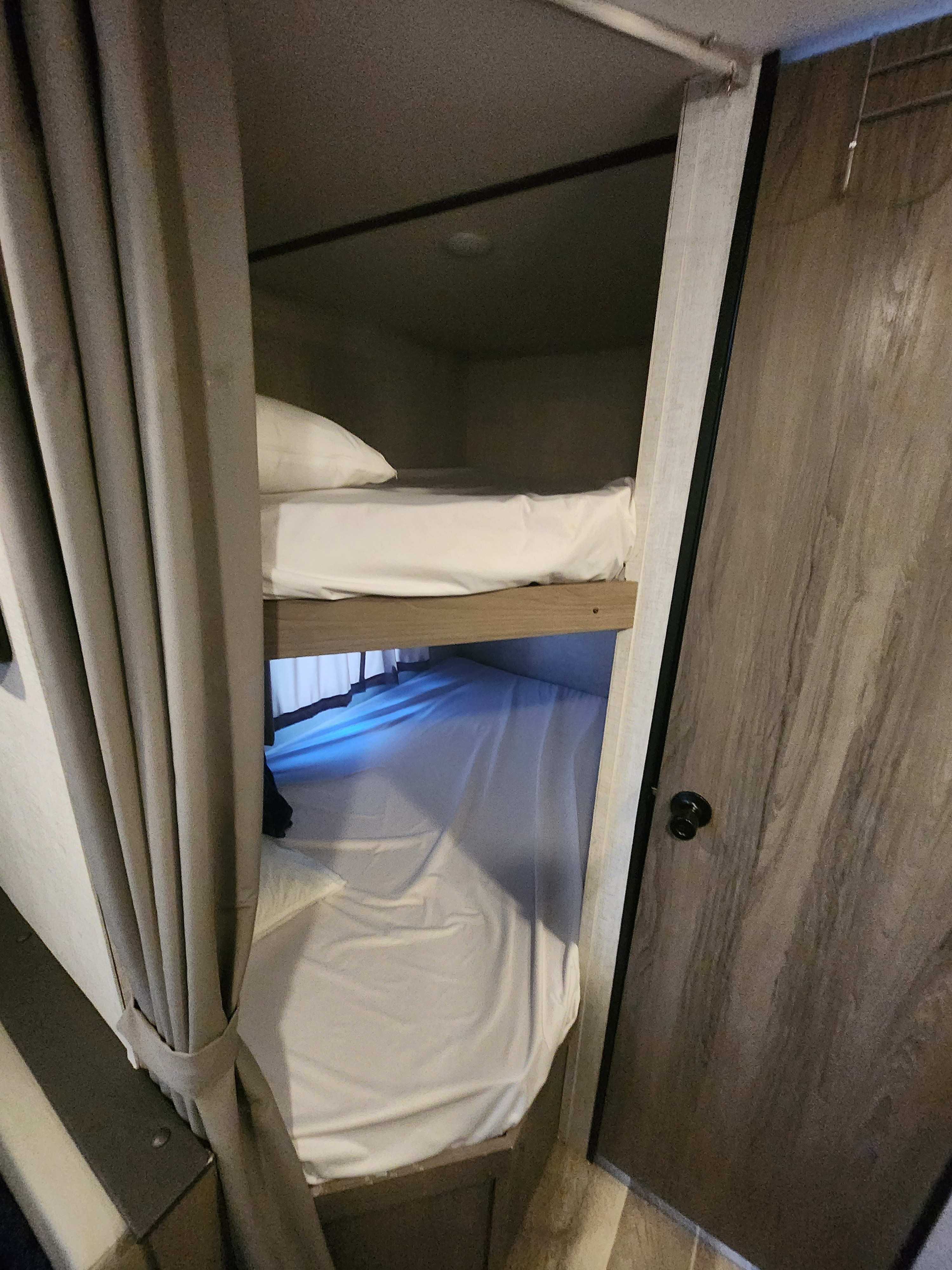 RV rental with cozy bunk beds. Two beds with white sheets, a pillow on top, and a grey privacy curtain on the left side.. Gulf Stream Ameri-Lite 2022