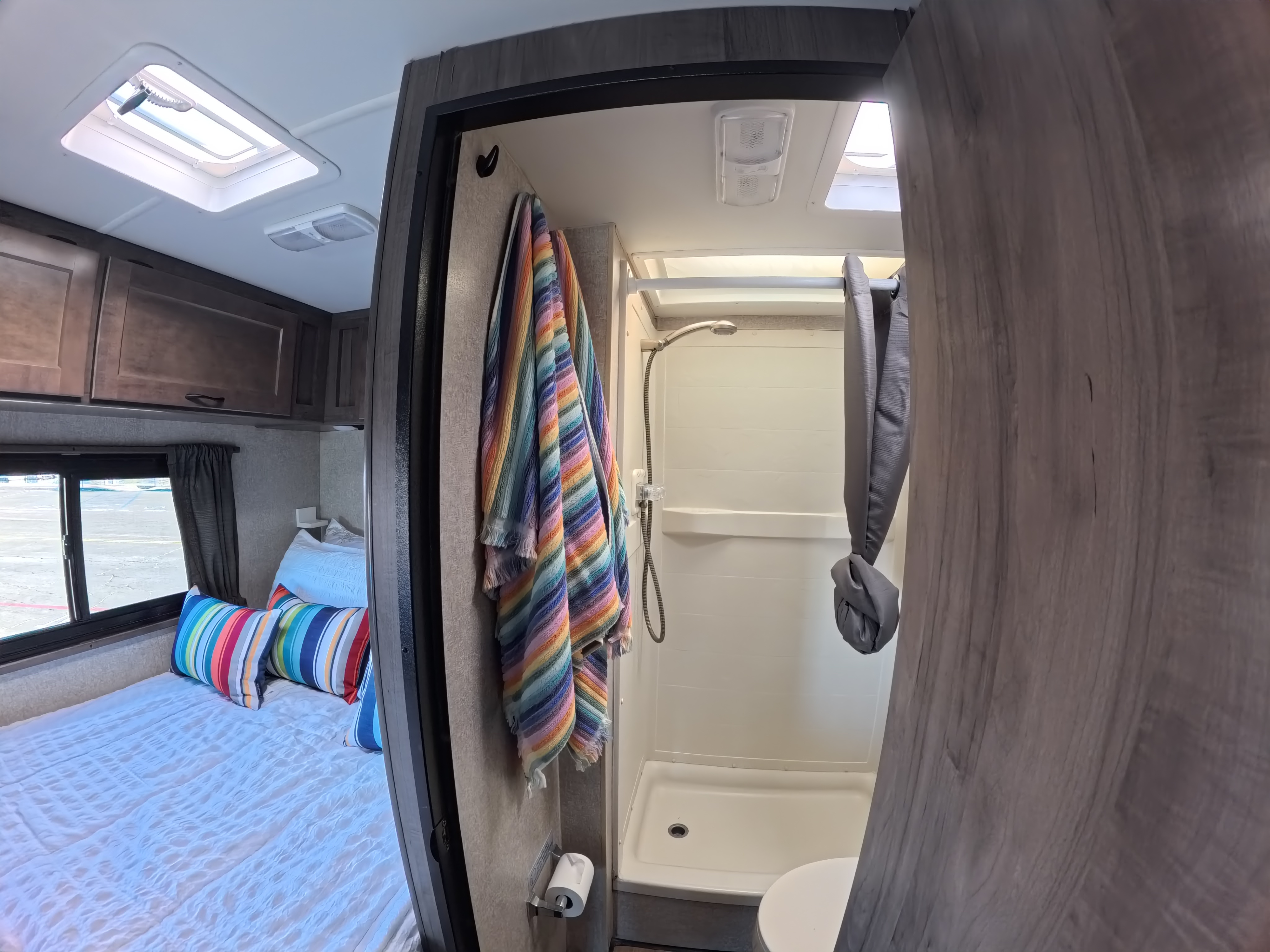 Cozy RV rental interior featuring a bedroom with vibrant striped pillows and an open door to a compact bathroom with a shower.. Winnebago Minnie Winnie 2020