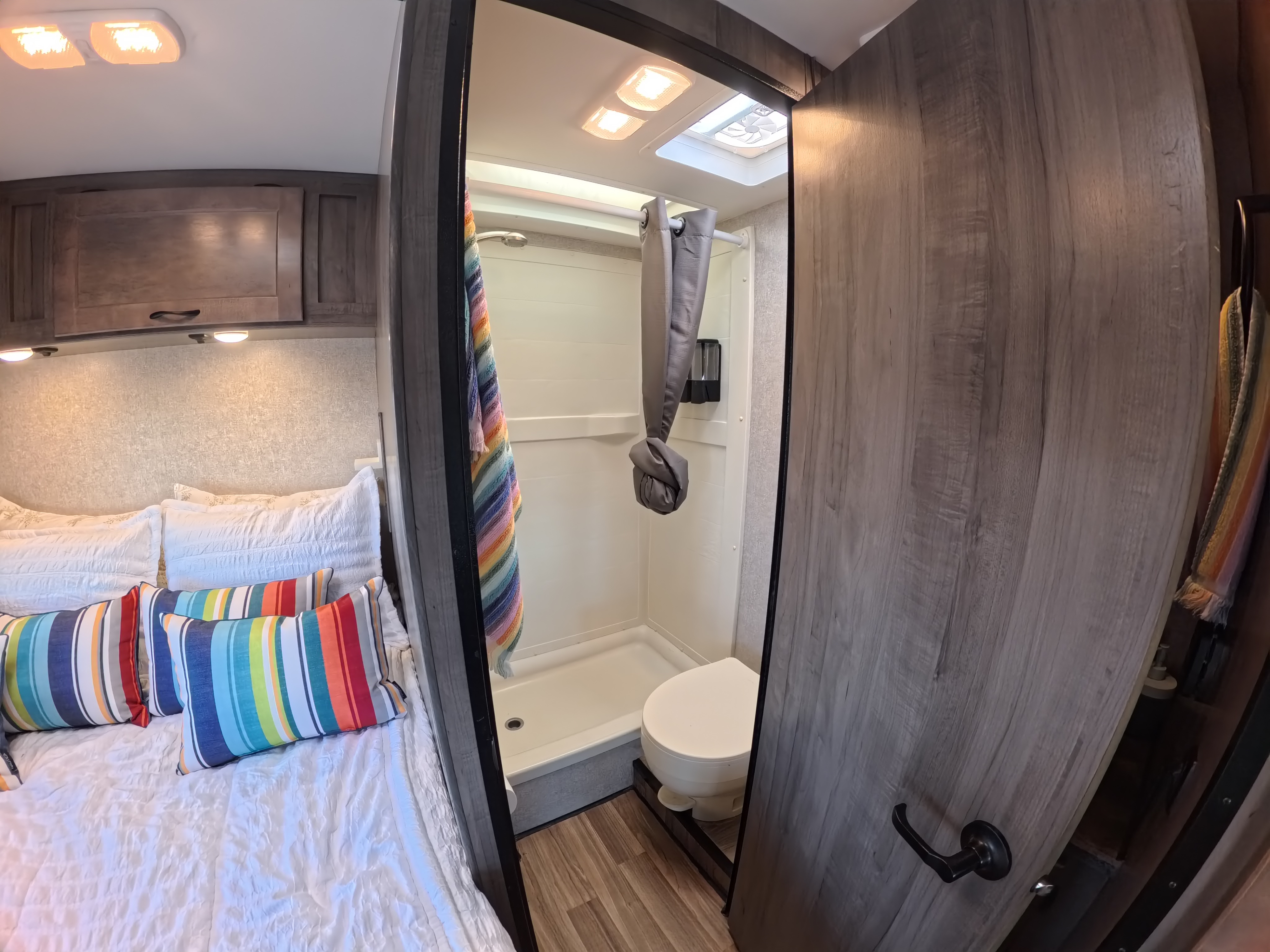 Cozy RV rental bedroom with colorful pillows and a compact bathroom featuring a shower and toilet.. Winnebago Minnie Winnie 2020