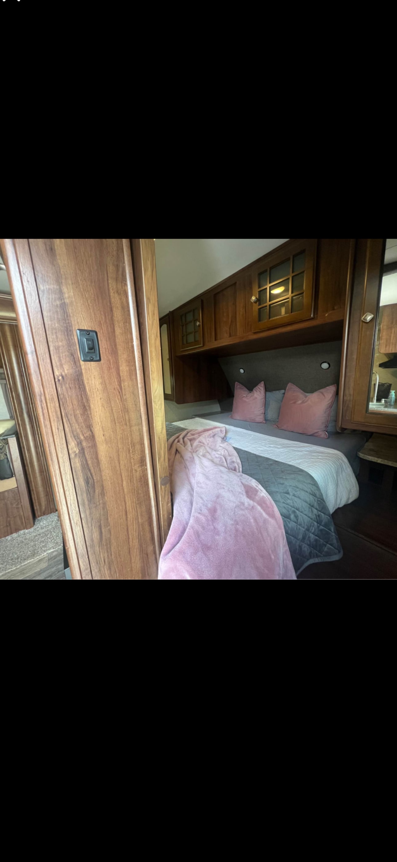 Cozy RV rental bedroom featuring a comfortable bed with pink pillows, a soft pink blanket, and elegant wooden cabinets.. Heartland RVs North Trail Caliber Edition 2017