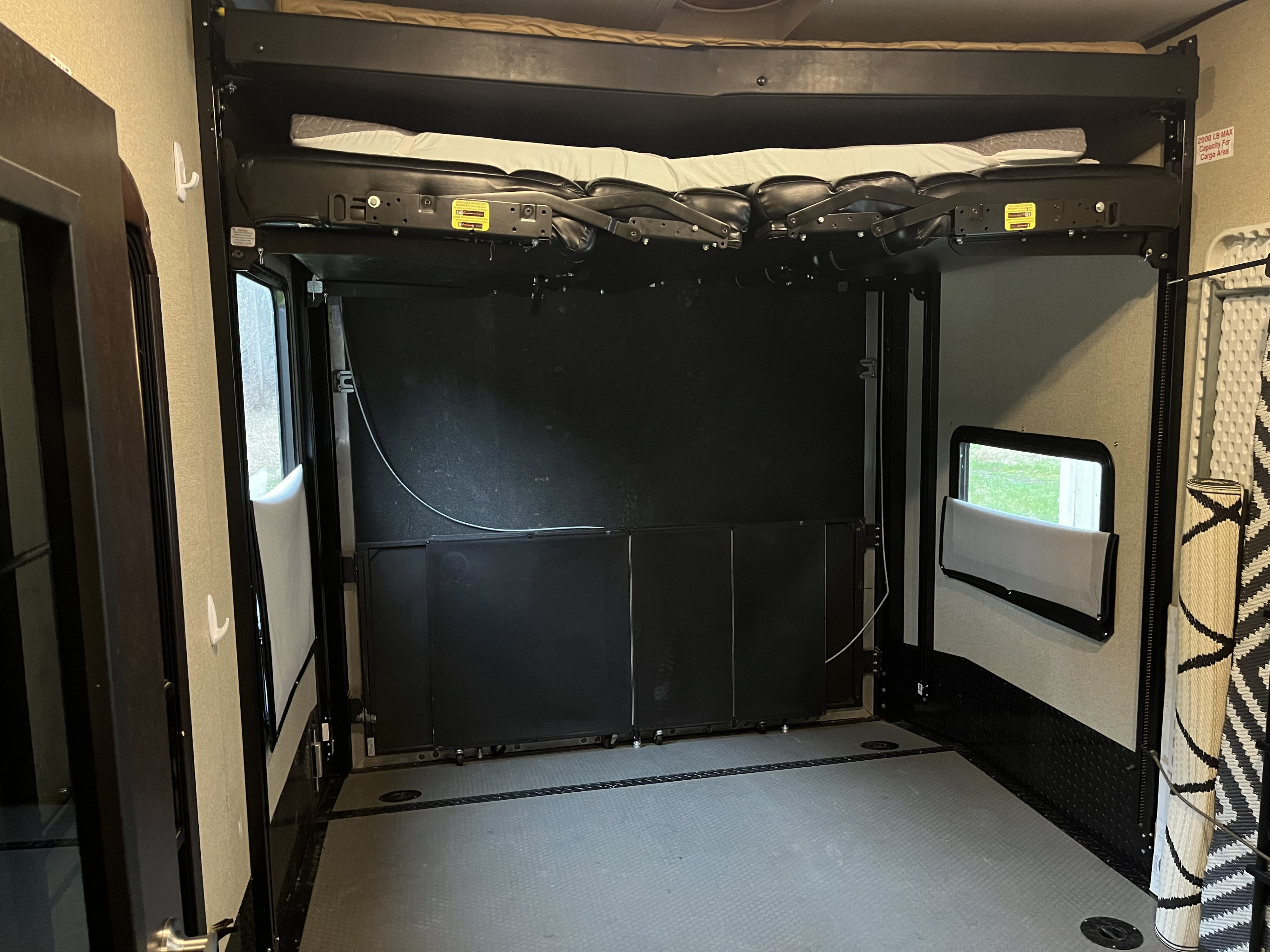 RV rental toy hauler interior showing a spacious cargo area with electric bunk bed and fold-down sofa.. Keystone Carbon 2018