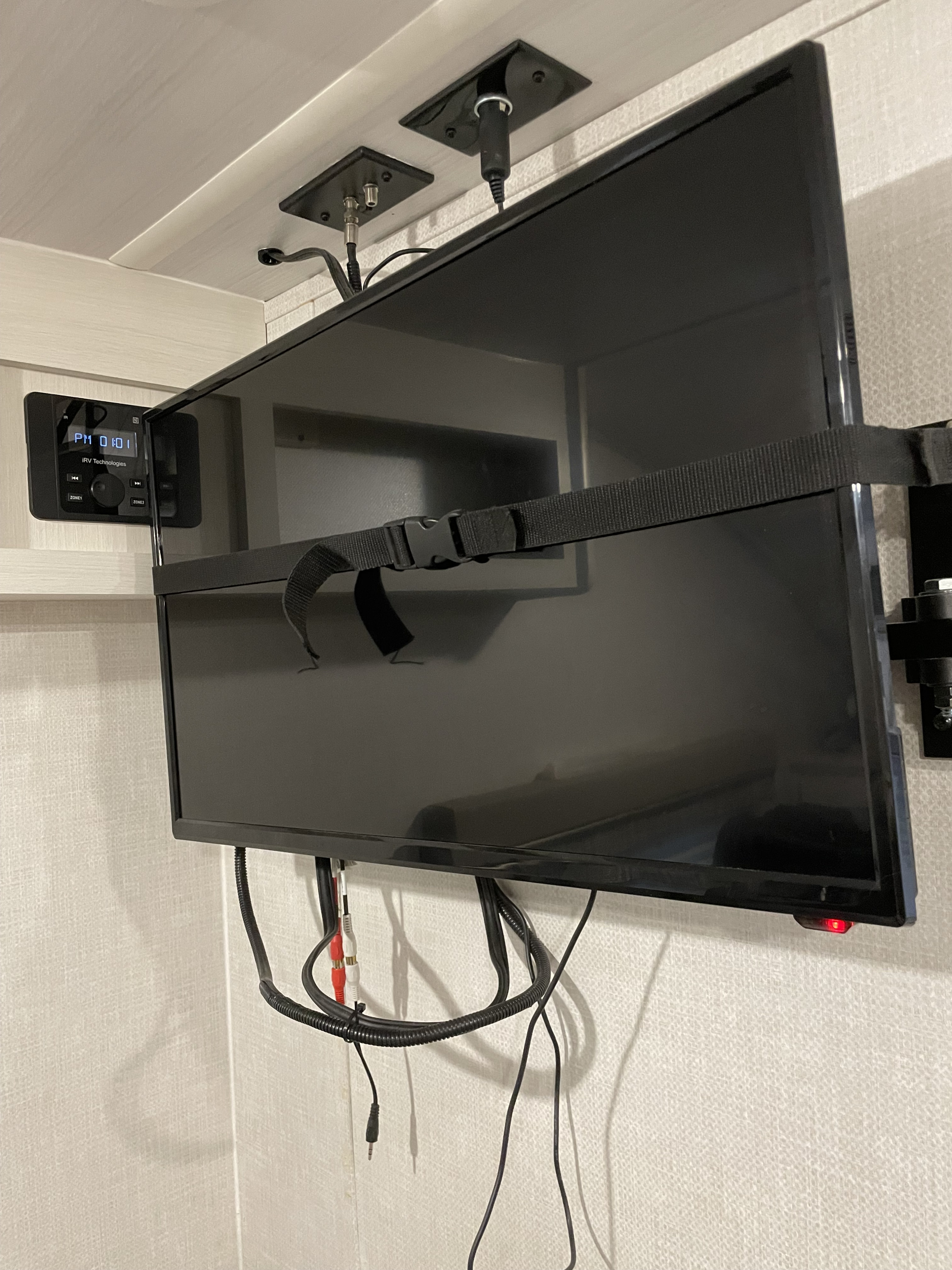 Inside an RV rental: A mounted TV is secured by a strap, next to an IRV Technologies stereo system and visible cables.. Forest River R-Pod 196 2022