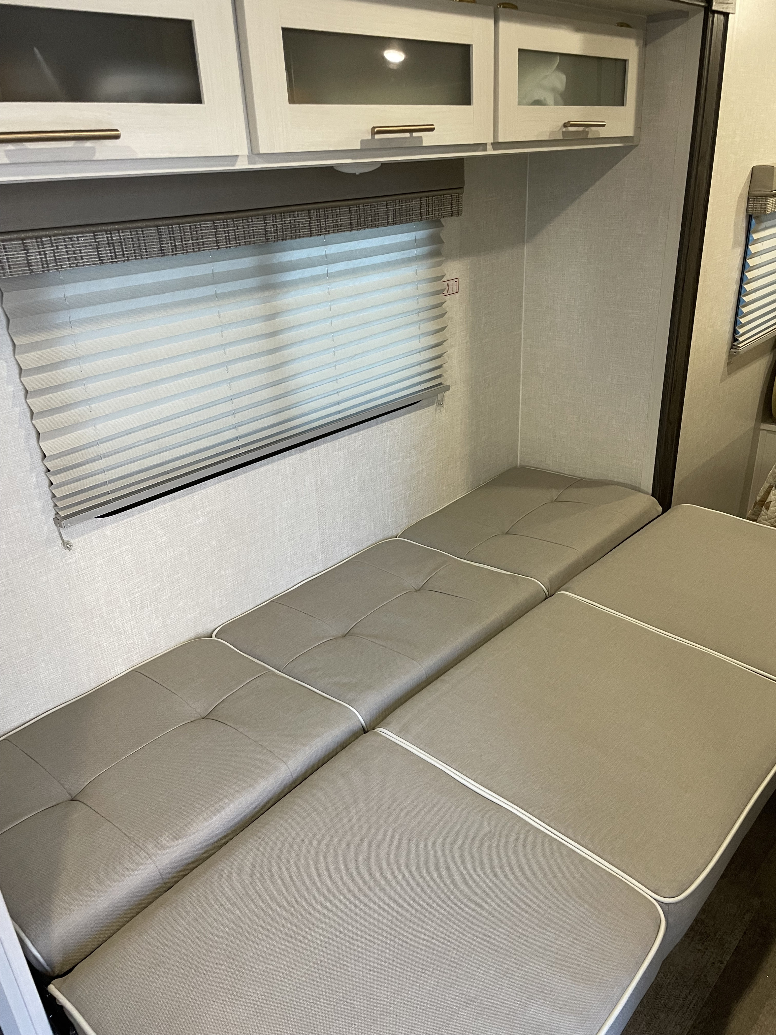 RV rental living area featuring light gray cushions for a convertible bed/dinette, modern overhead cabinets, and a window.. Forest River R-Pod 196 2022