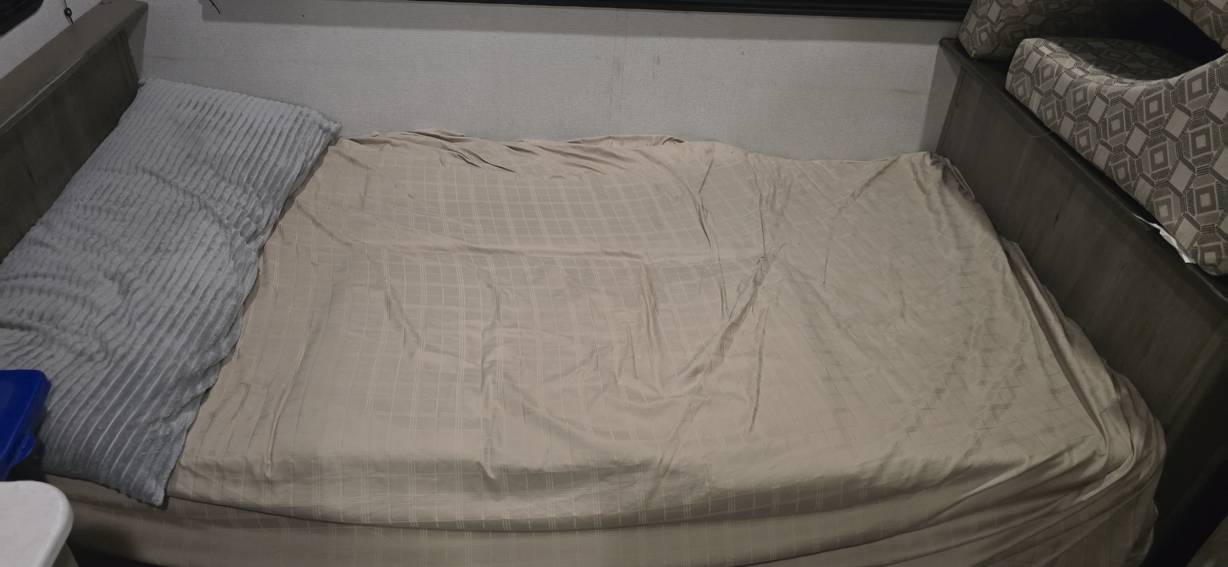 RV rental bed with a soft grey pillow and beige checkered sheet, ready for a comfortable night's sleep during your travels.. Keystone RV Springdale 2021