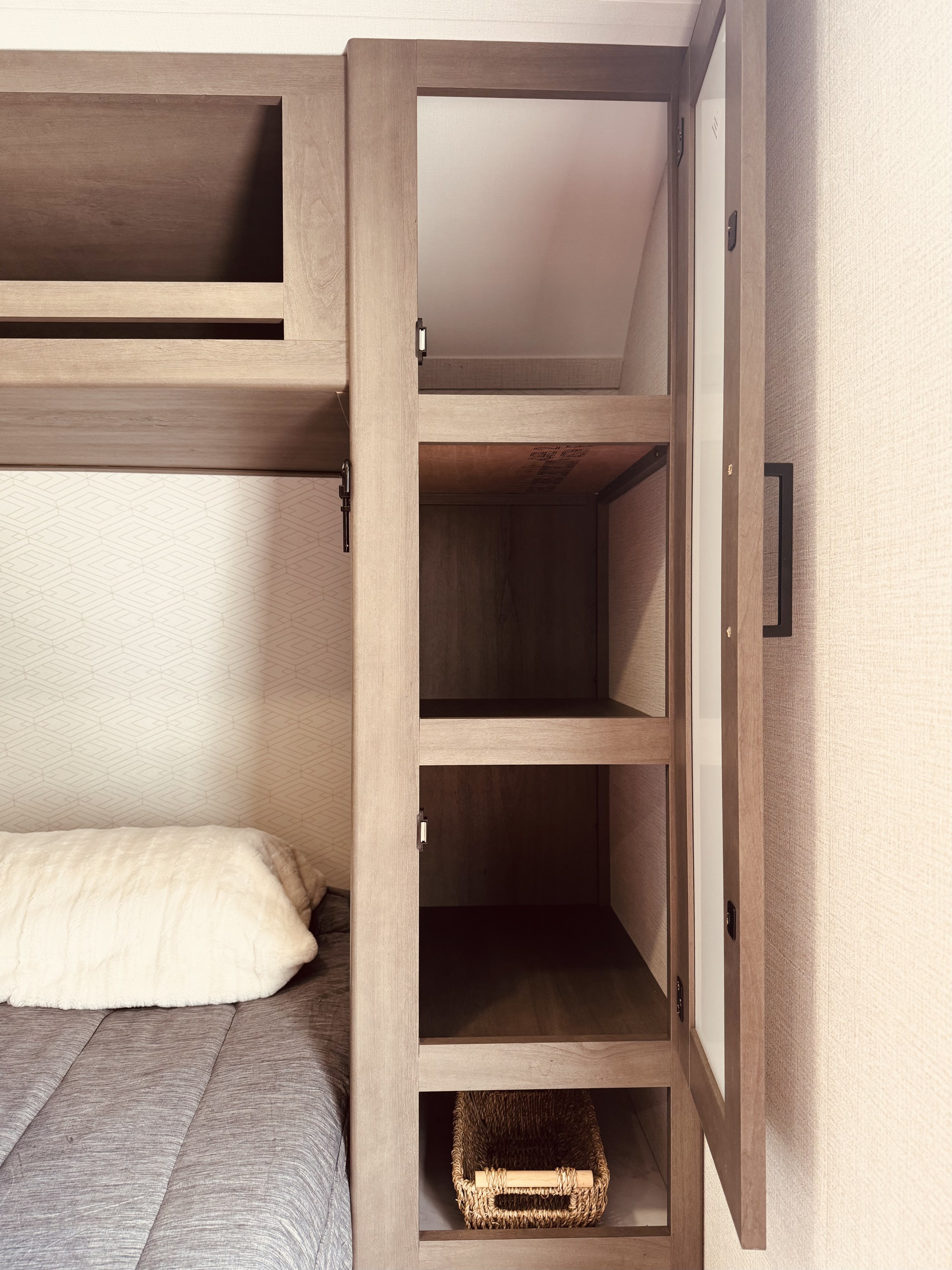 RV rental sleeping area featuring a bunk bed with soft bedding and an open storage cabinet with shelves, ready for your travel essentials.. Grand Design Transcend One 2025