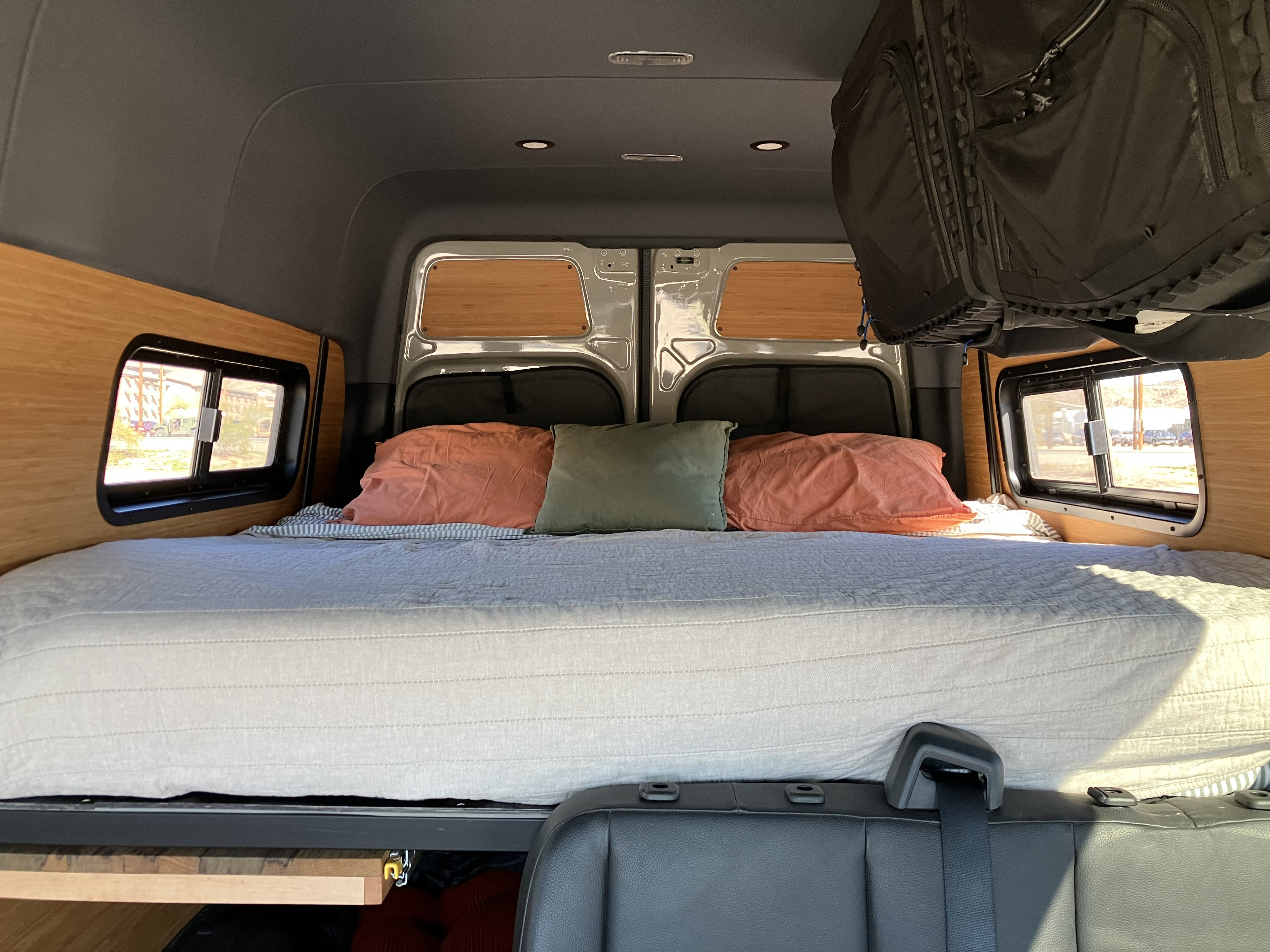 This RV rental offers a comfy bed with orange/green pillows, wood walls, side windows, and overhead lights for your journey.. Mercedes Sprinter 2024