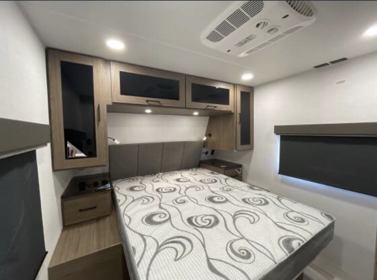 Spacious RV rental bedroom with a large bed, overhead storage, and AC unit for comfortable travels.. Alliance RV Delta 2024
