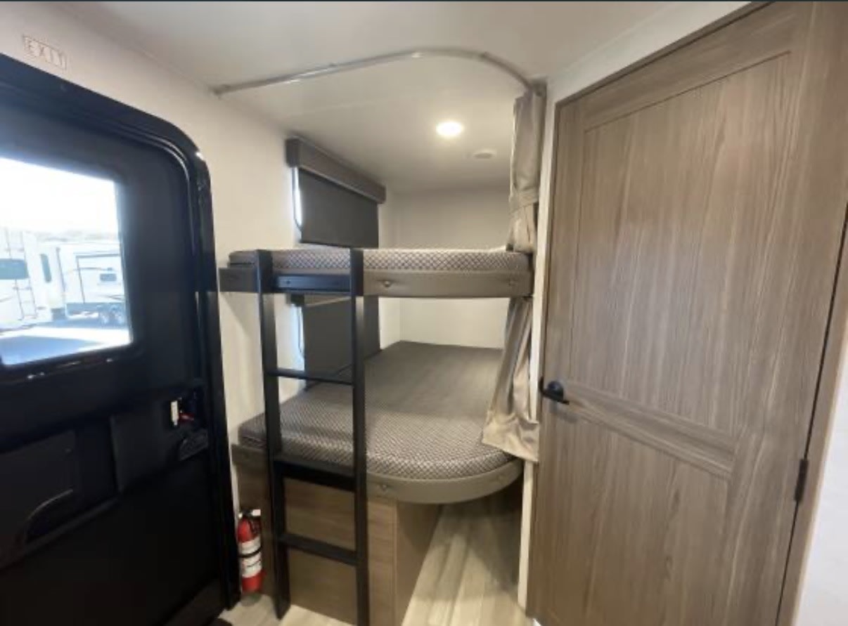Compact rv rental interior with sturdy bunk beds, ladder, and privacy curtain. A fire extinguisher is by the entry door.. Alliance RV Delta 2024
