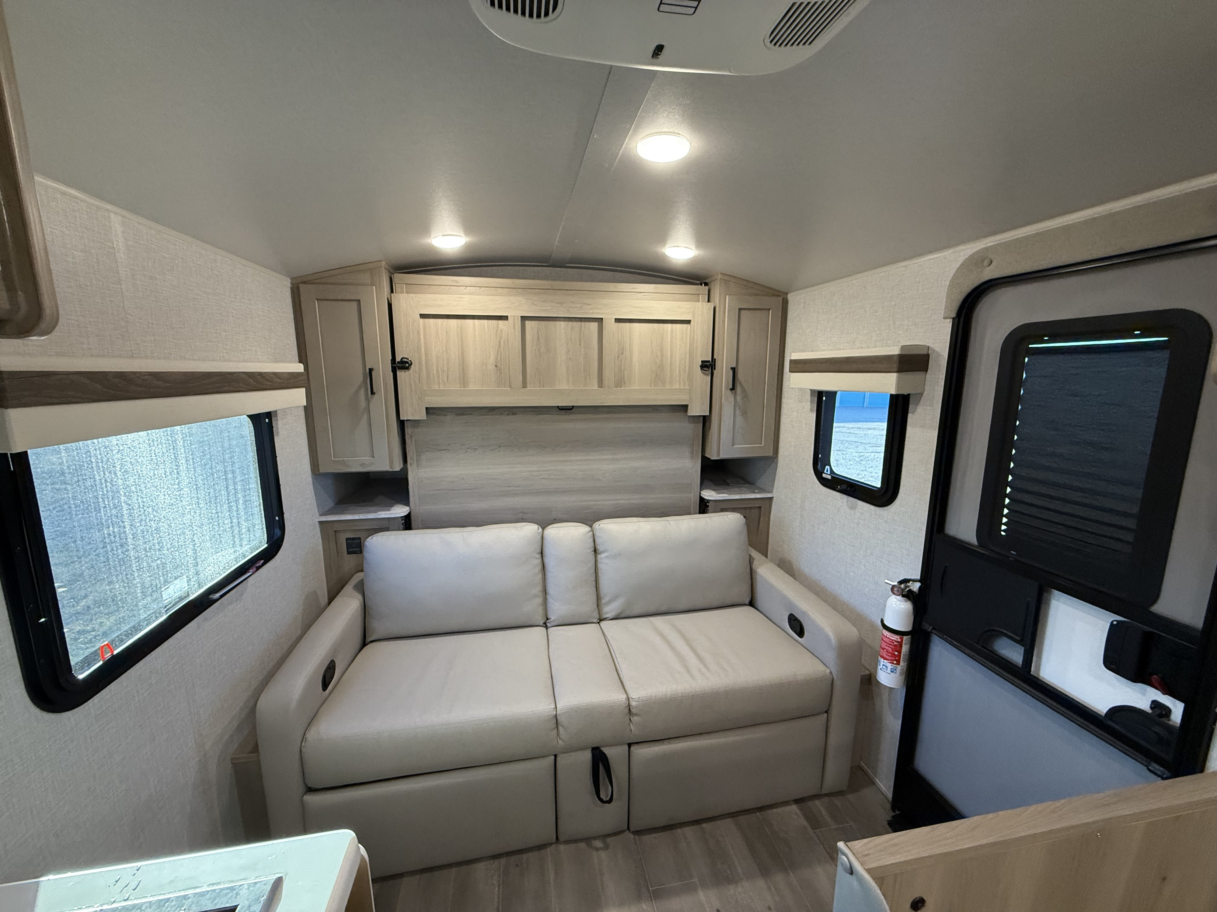 Cozy RV rental interior featuring a cream sofa bed, wood-look cabinets, windows, and an entry door with a fire extinguisher.. Forest River Rockwood Geo Pro 2023