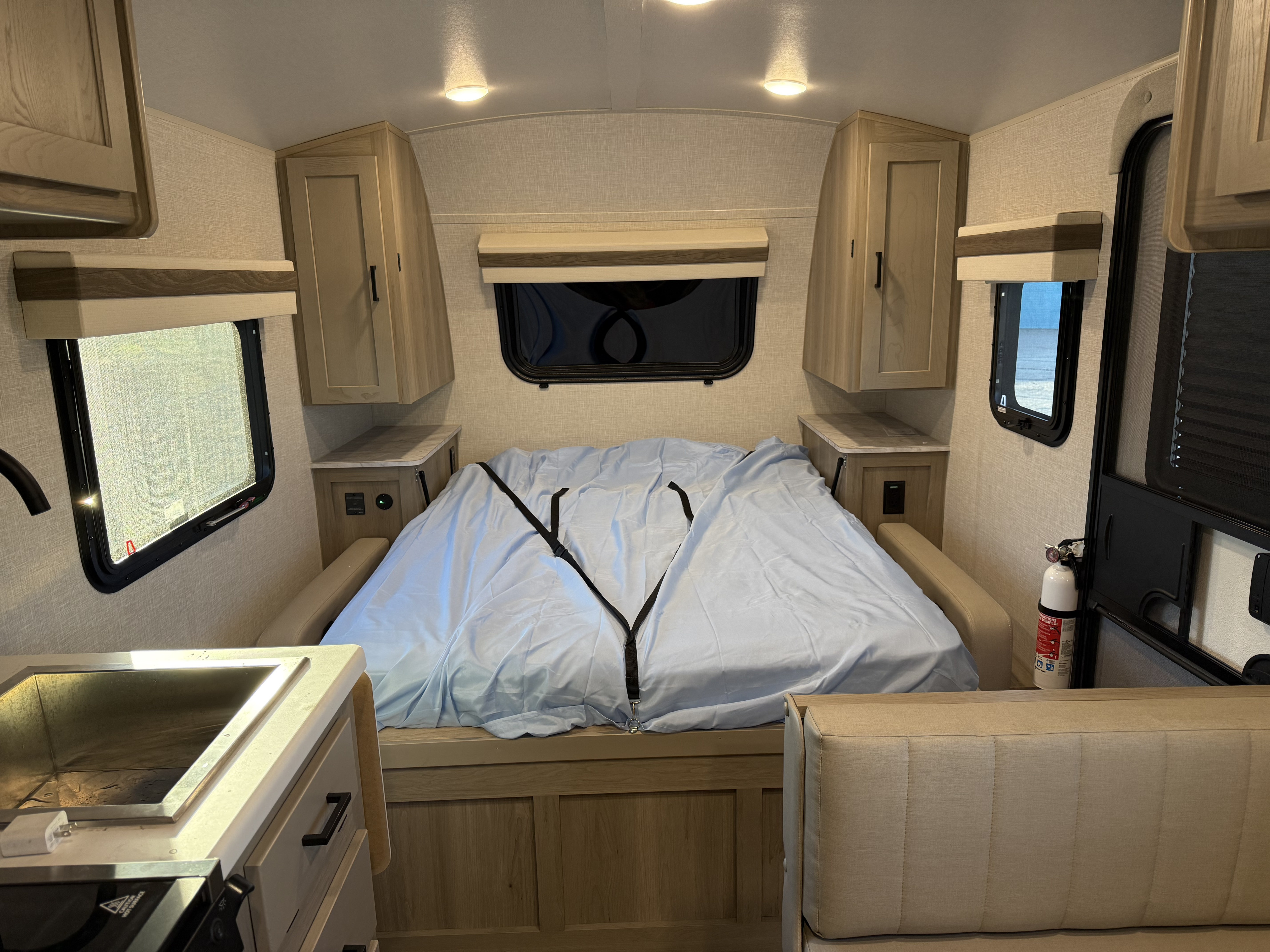 Cozy RV rental bedroom area with a bed, overhead storage, windows, and a compact kitchen corner for road trip comfort.. Forest River Rockwood Geo Pro 2023
