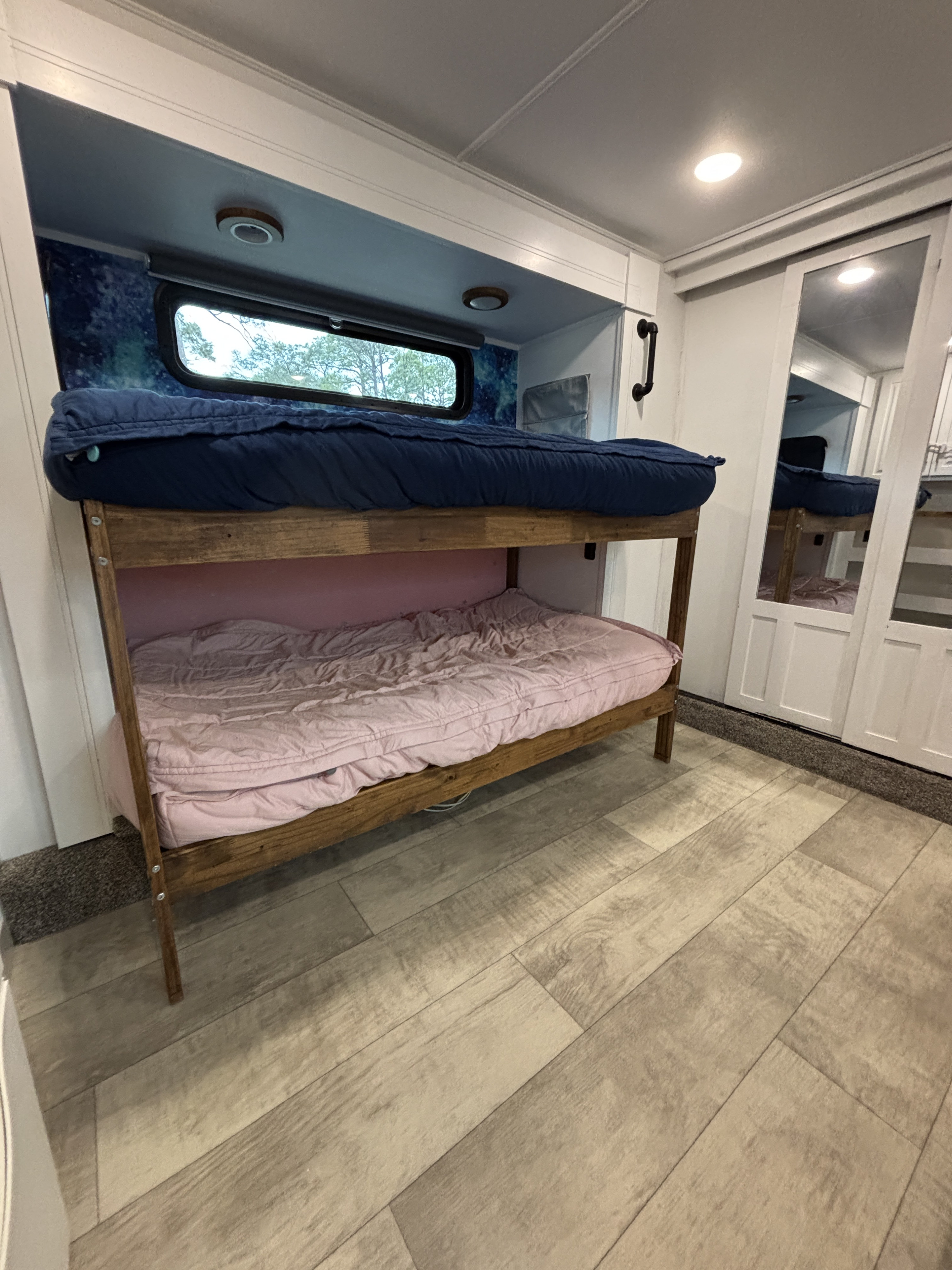 RV rental interior features custom wooden bunk beds with blue and pink bedding, a window, and light wood-look flooring.. Grand Design Momentum 2021