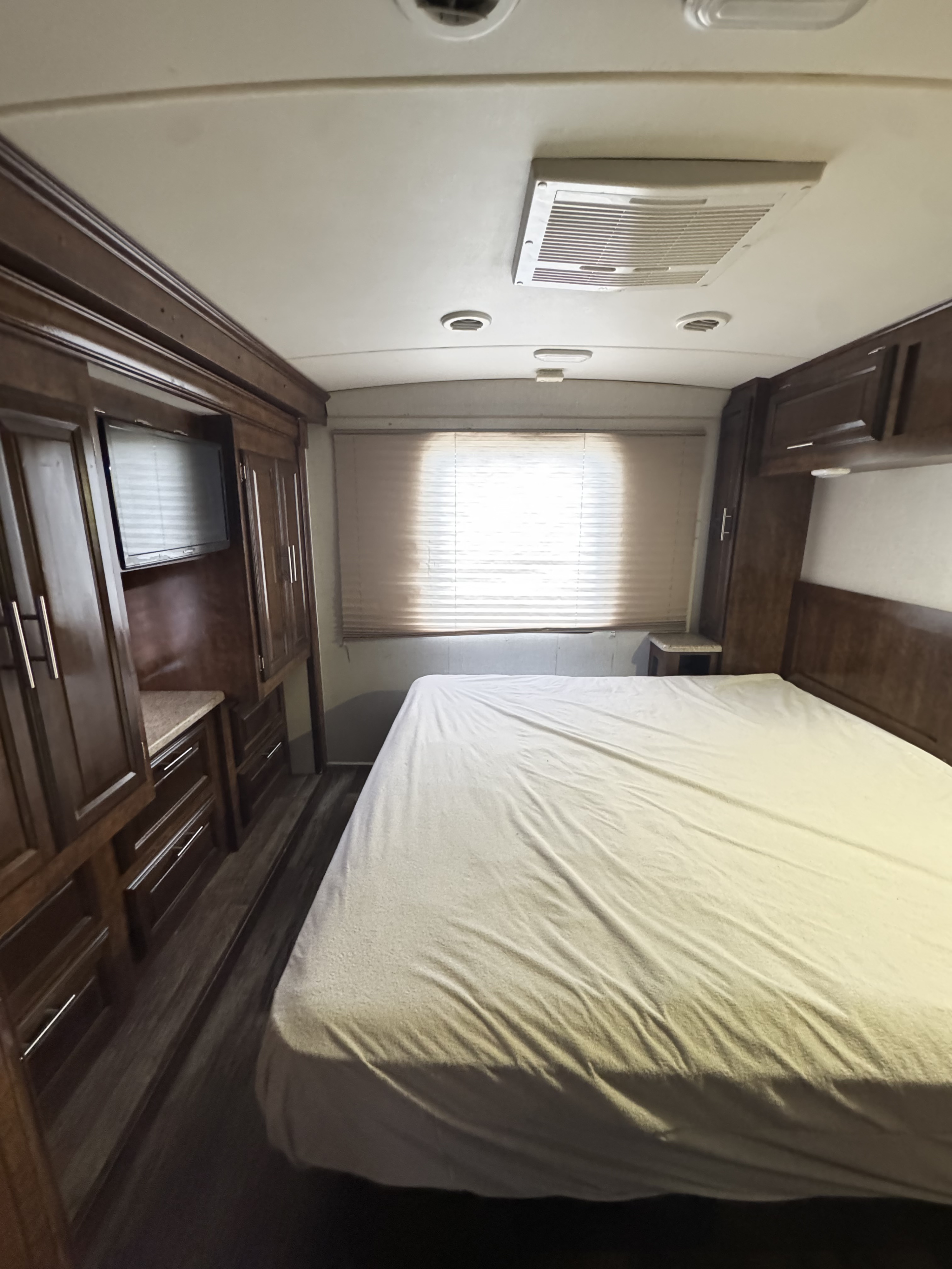 Inside an RV rental: a cozy bedroom with bed, window blinds, storage cabinets, and a wall-mounted TV.. Forest River FR3 2017