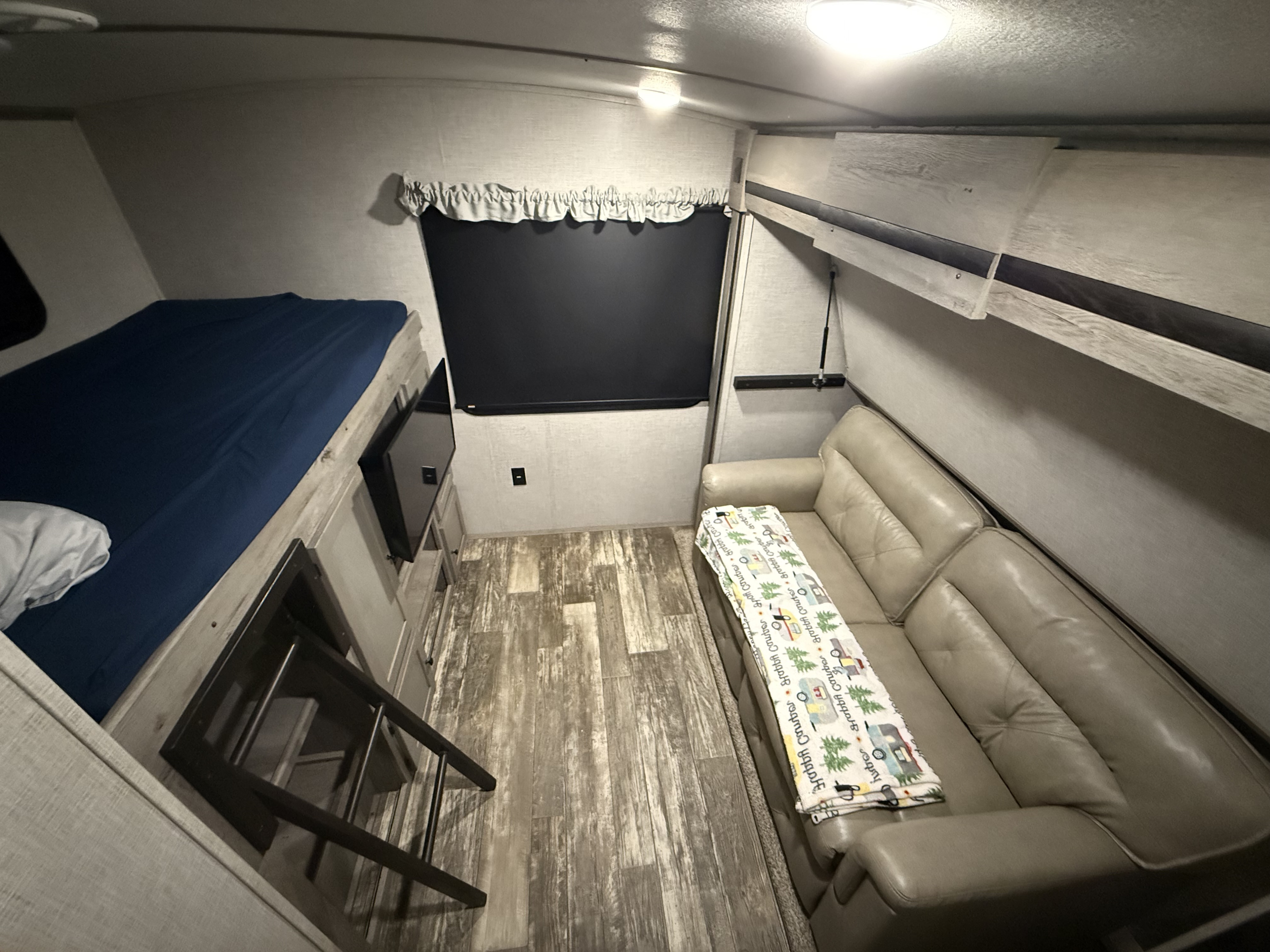 RV rental bunkhouse view: a blue-sheeted bunk bed with ladder, a cozy sofa with a camper-themed blanket, and a TV.. Keystone RV Outback 2020