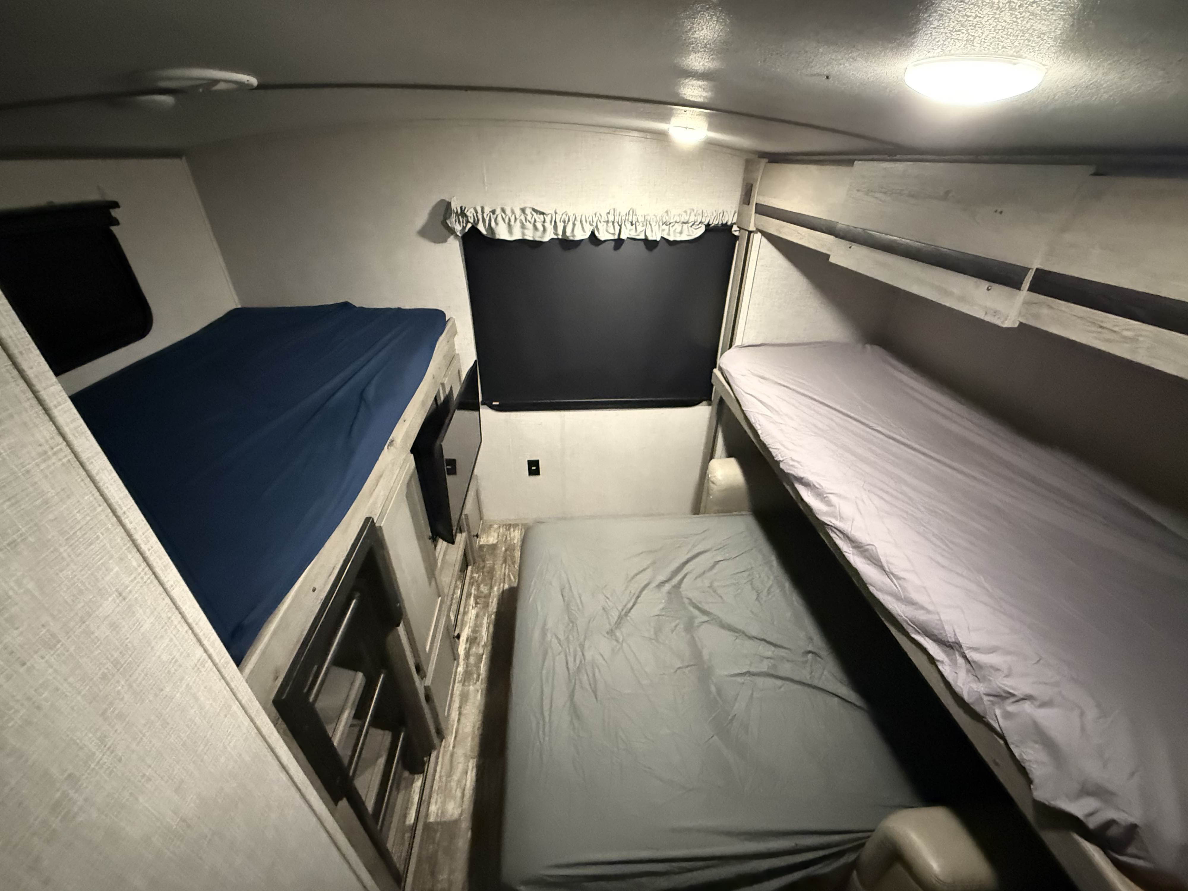 RV rental interior shows two sets of bunk beds: blue-sheeted on the left, light grey on the right. A functional camper sleeping area.. Keystone RV Outback 2020