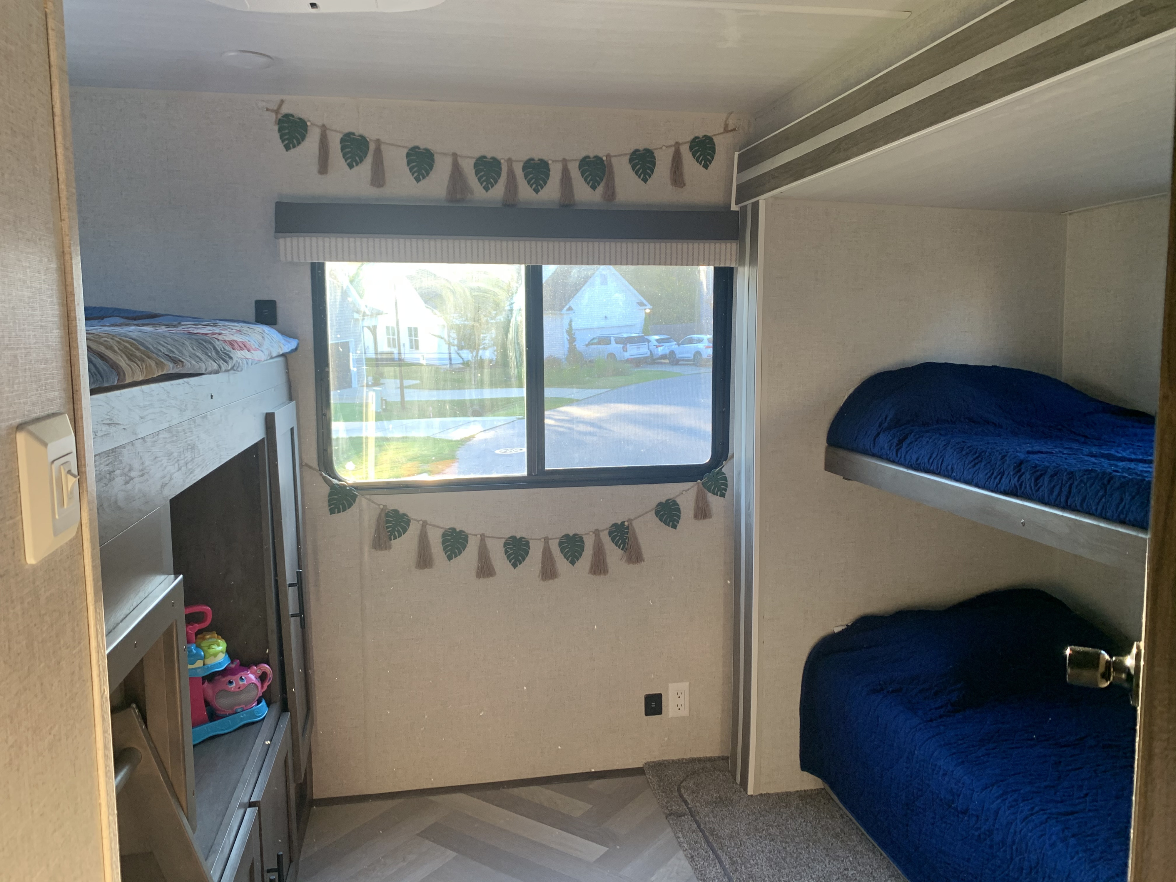 RV rental interior: cozy bunk beds, window with street view, and playful leaf garland create a welcoming kids' sleeping area.. Forest River Wildwood 2021