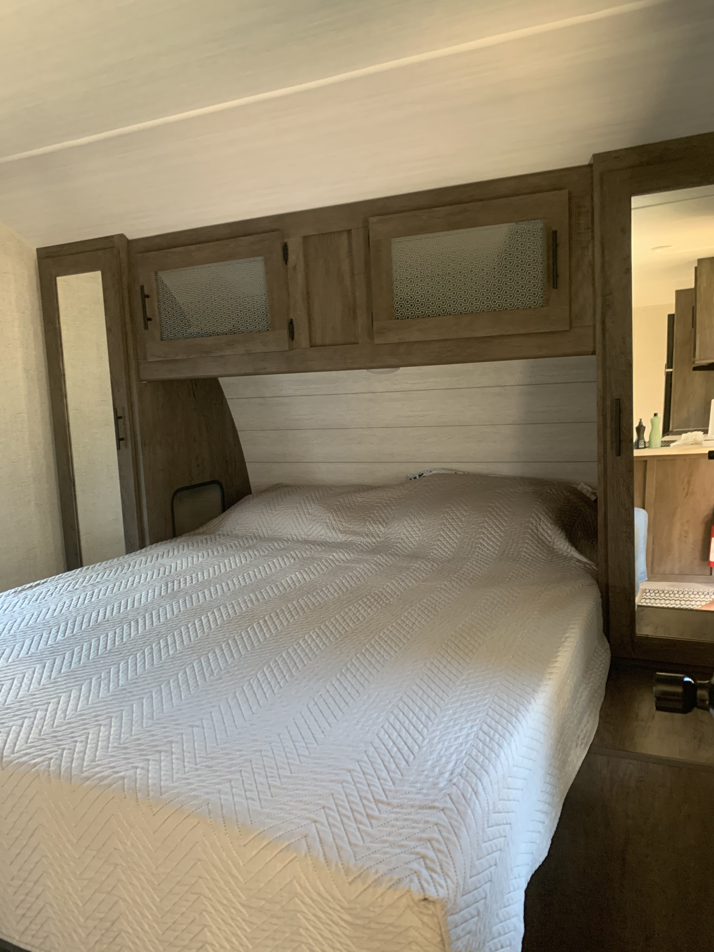 Quilted bed in a modern RV rental bedroom with overhead cabinets and side mirrors, offering a compact, comfortable space.. Forest River Wildwood 2021