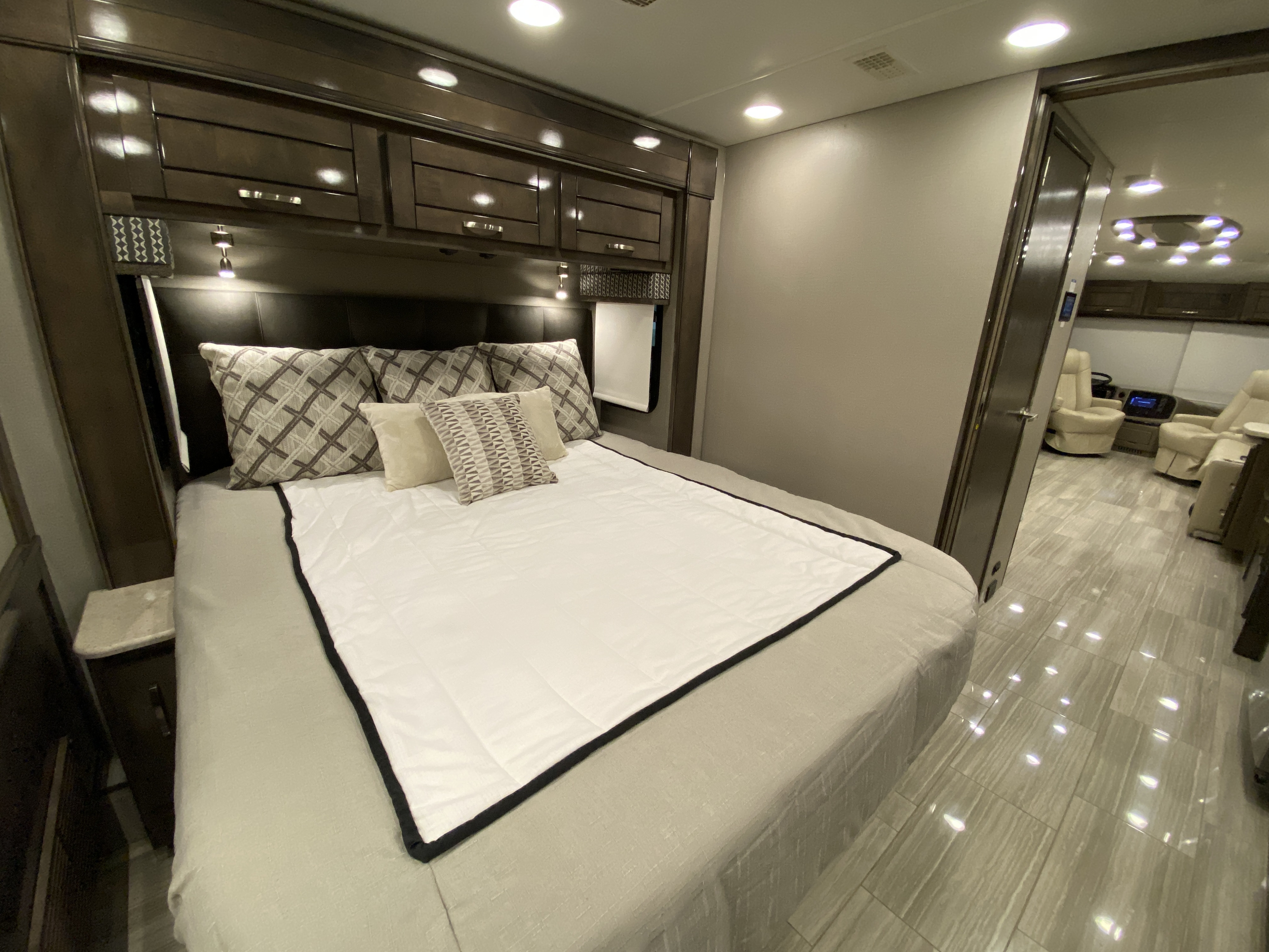 Modern RV rental bedroom interior with a neatly made bed, overhead cabinets, and a peek into the front cabin area.. Entegra Coach Reatta 2021